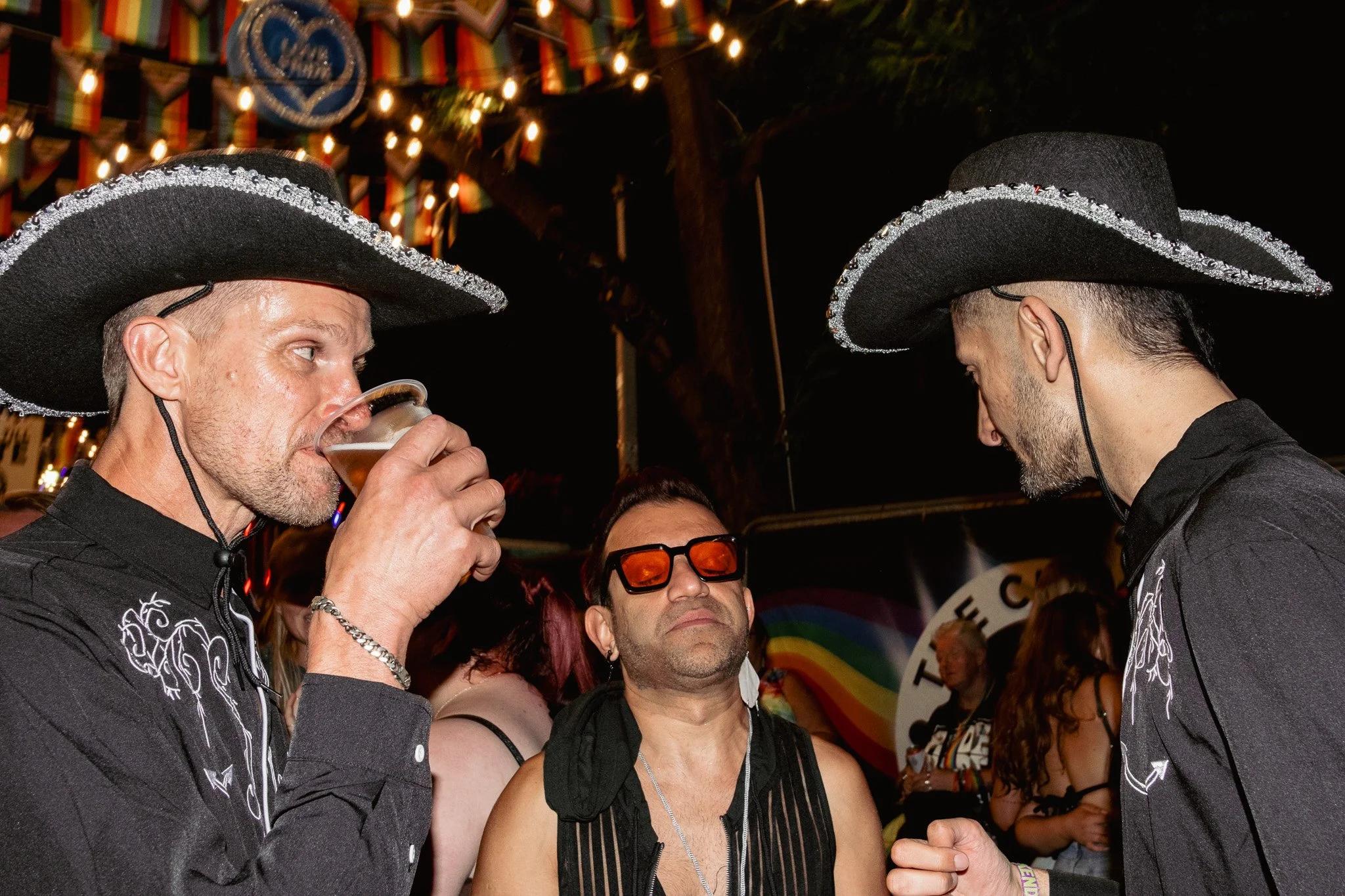 Three men wearing traditional Mexican sombreros at a lively celebration, with colorful lights and decorations in the background.