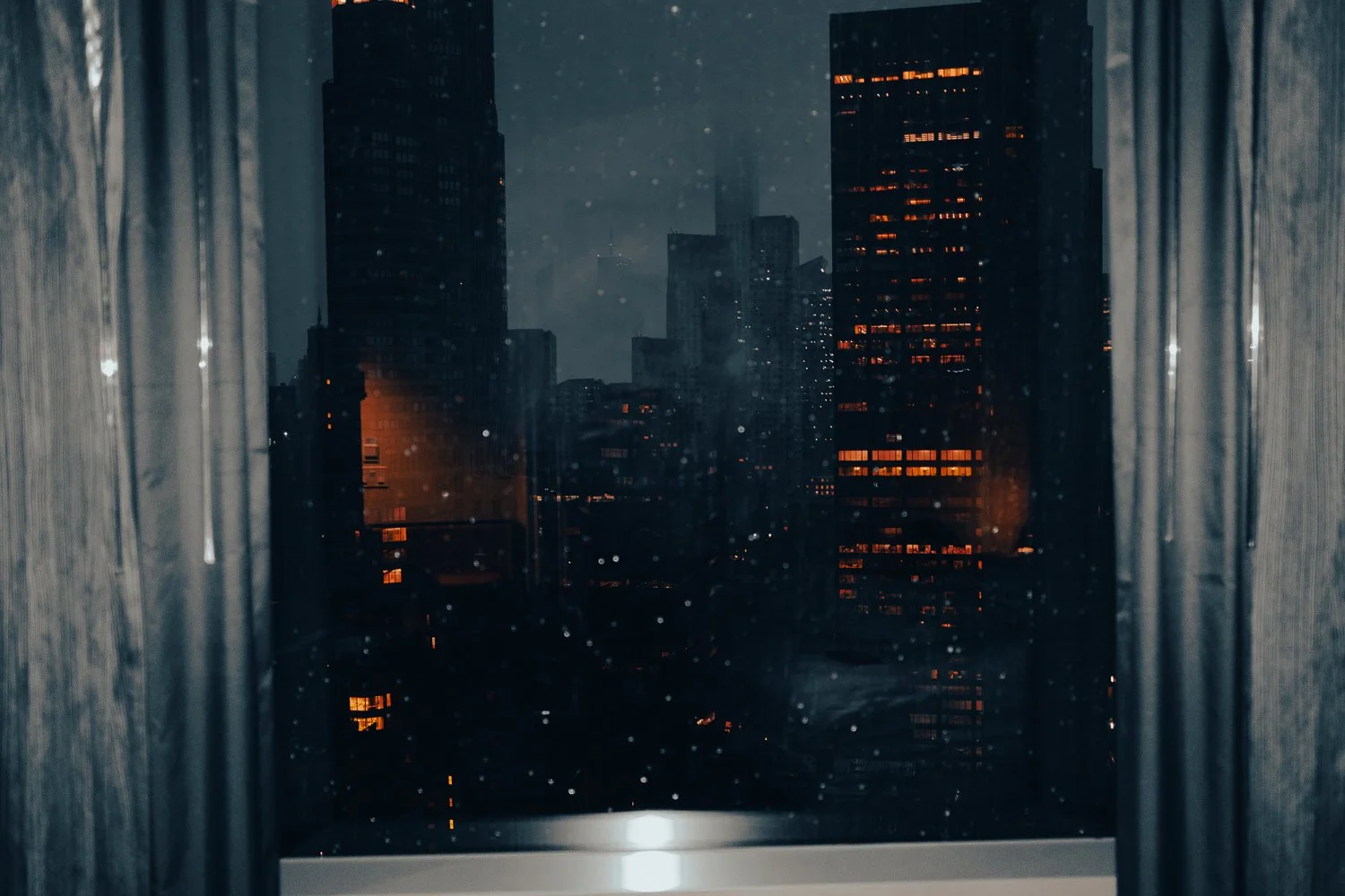 Night view of city buildings through a window with rain droplets and curtains on both sides.