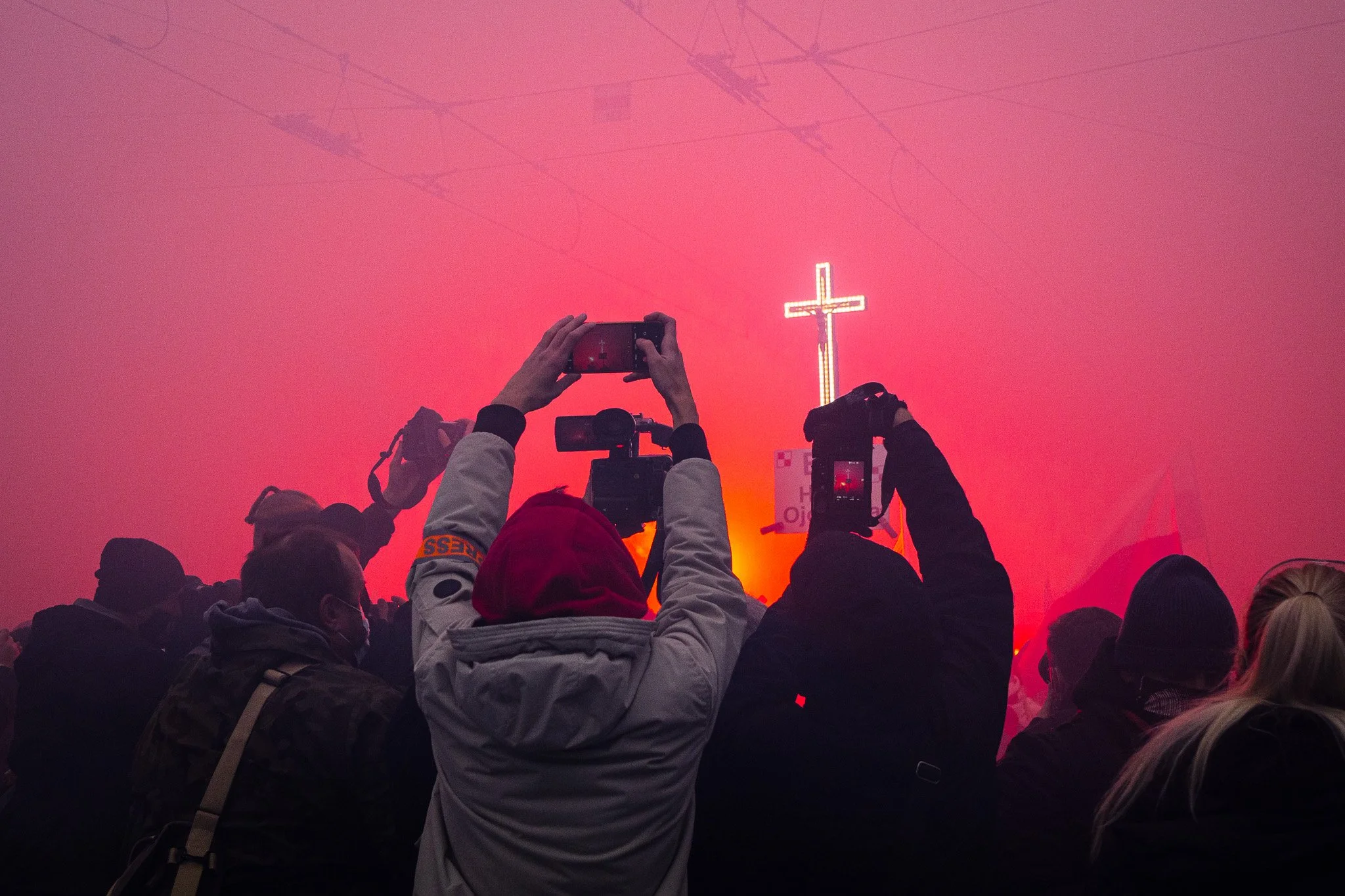 Crowd of people taking photos of a lit cross during a smoke-filled event.