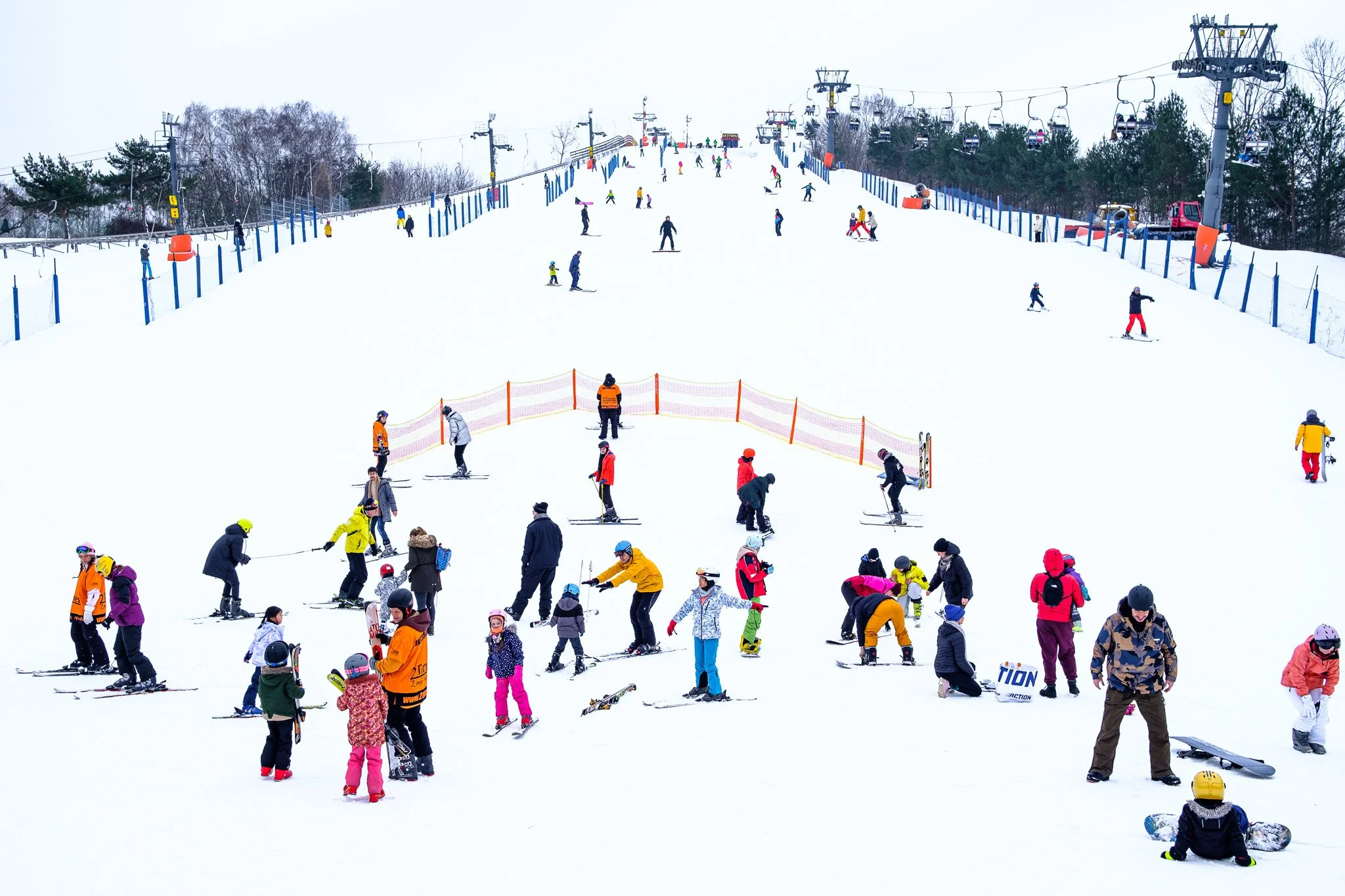 People skiing and snowboarding on a snow-covered slope at a ski resort, with ski lifts and trees in the background.