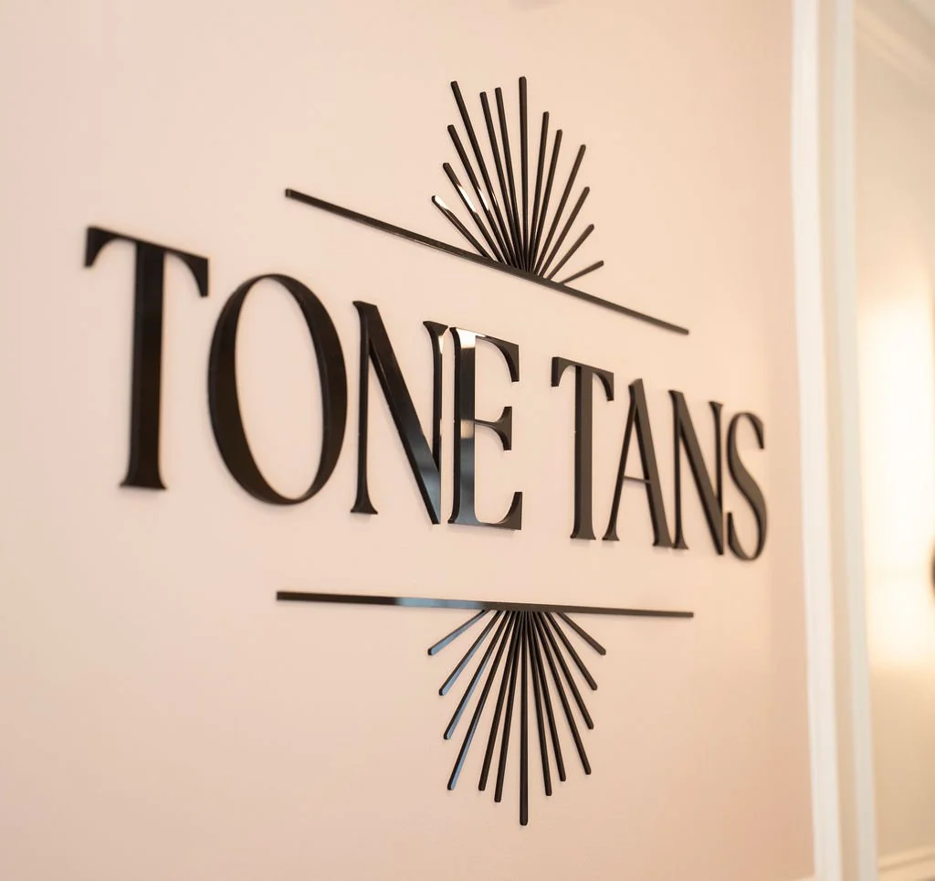 Decorative wall sign reads 'TONE TANS' with black 3D letters, flanked by starburst designs above and below, on a beige wall.
