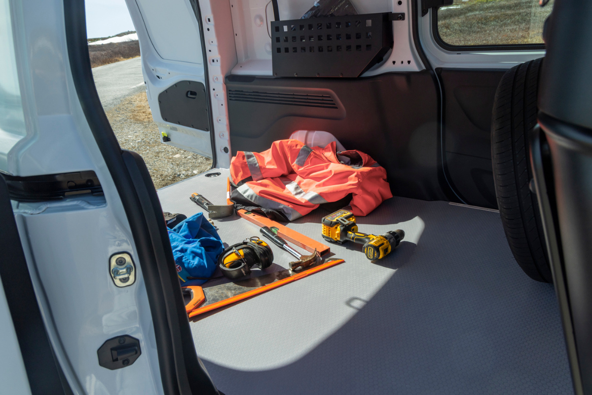 Tools, safety vest, and equipment inside the cargo area of a van, with an open door and a roadside view outside.
