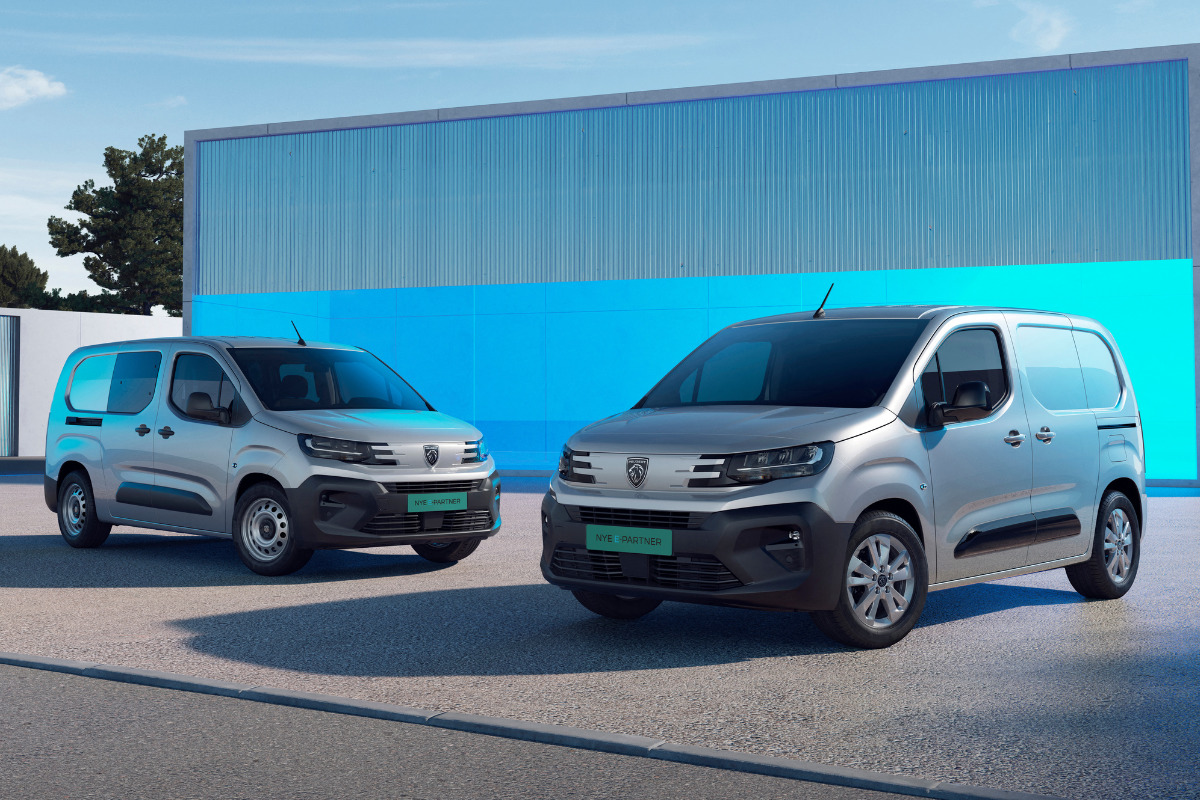 Two silver vans parked in front of a modern building with a blue wall, under a partly cloudy sky.