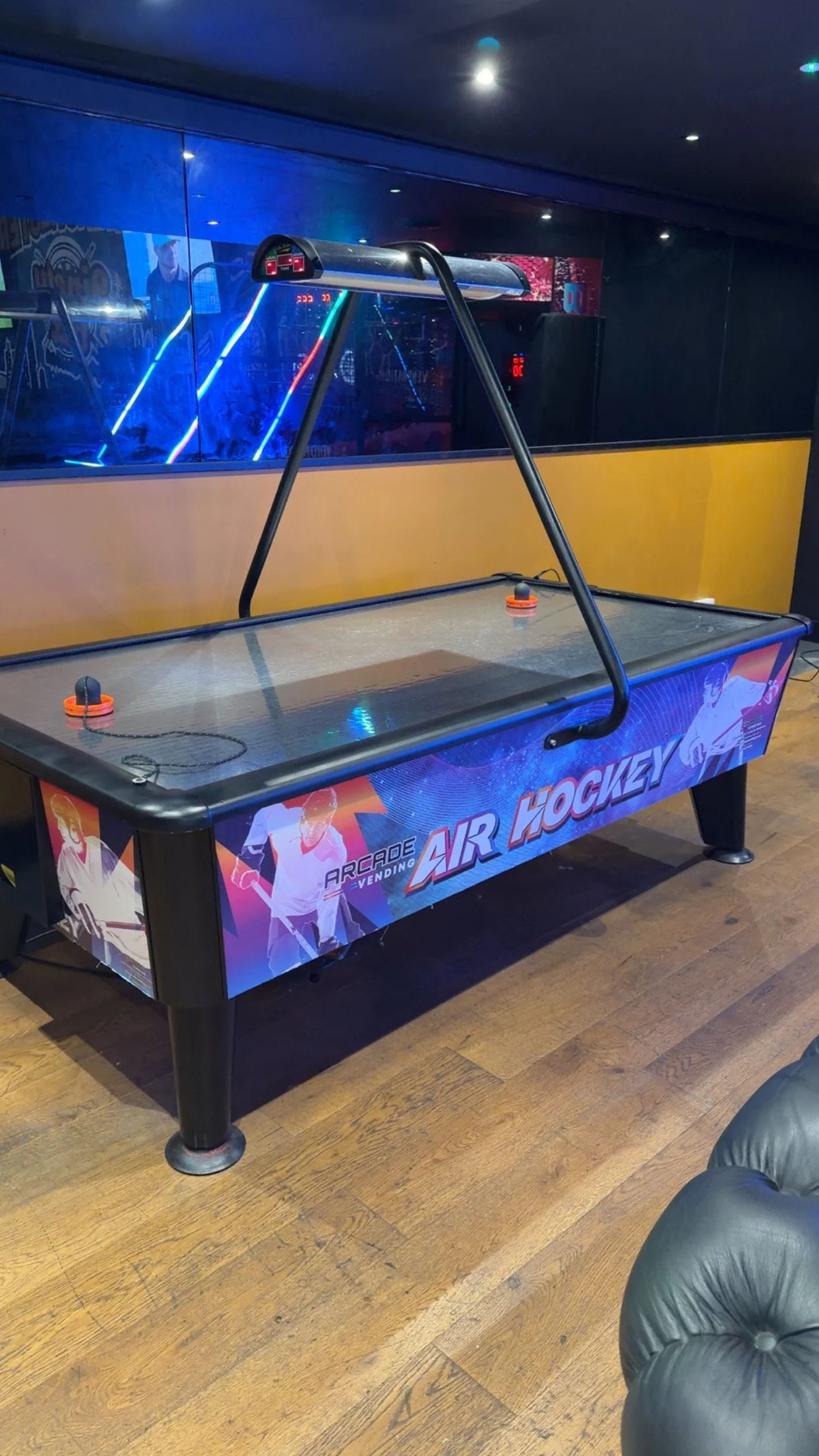A bright pink arcade-style air hockey table with overhead electronic scoreboard.