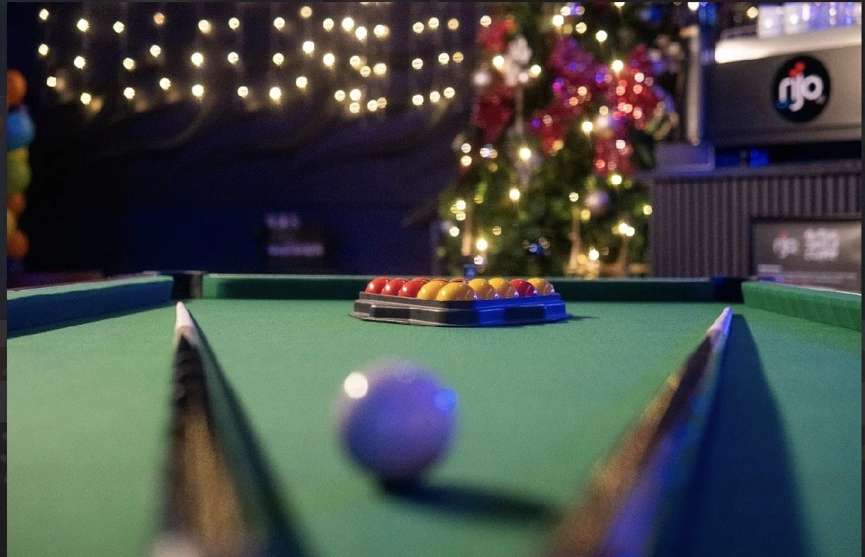 A black and purple pool table with cues resting on the sides.