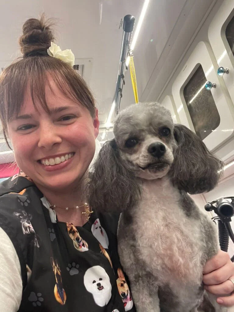 mobile groomer smiling with grey and white miniature poodle