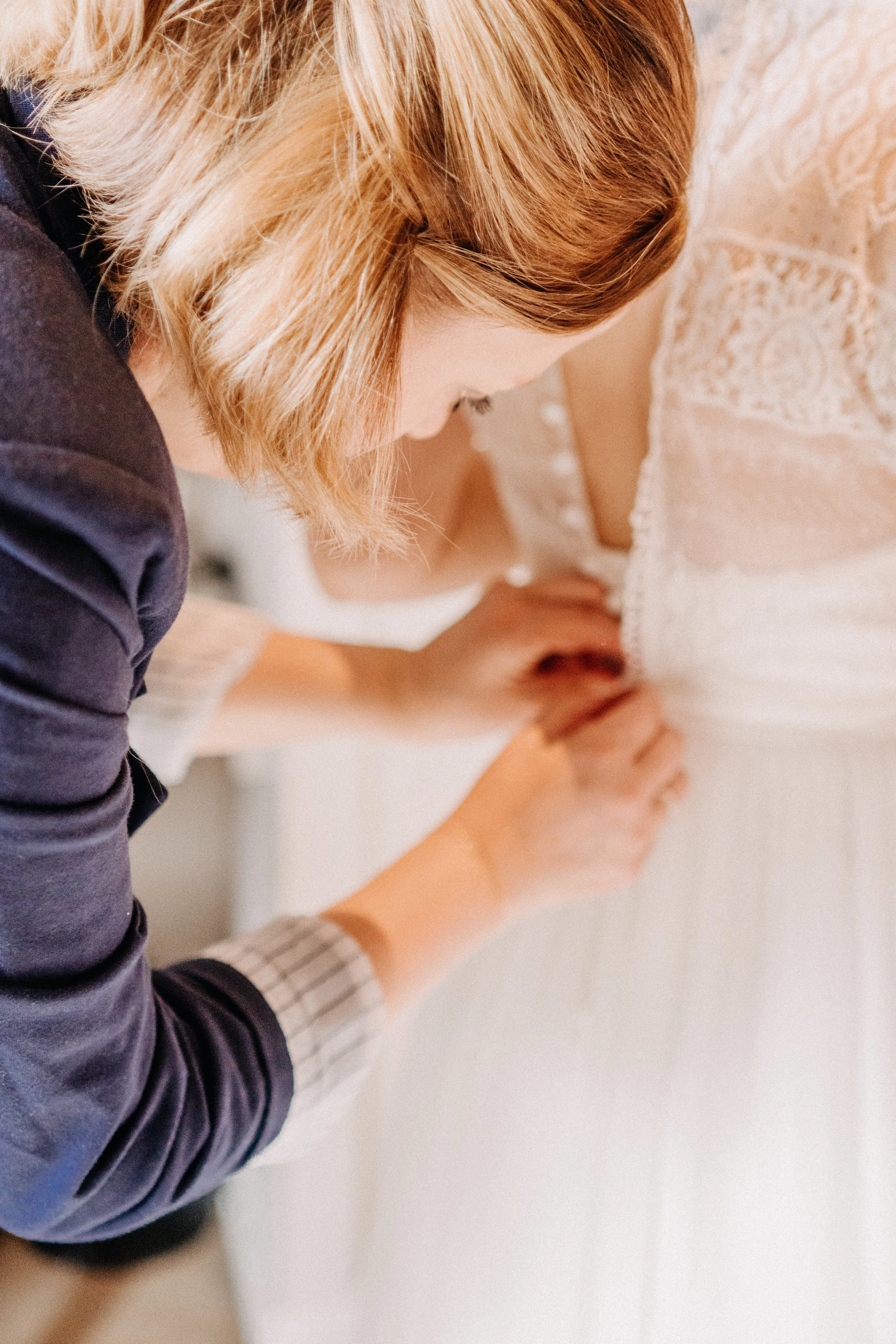Eine Frau hilft einer anderen Frau dabei, einen weißen Brautkleid zu richten.