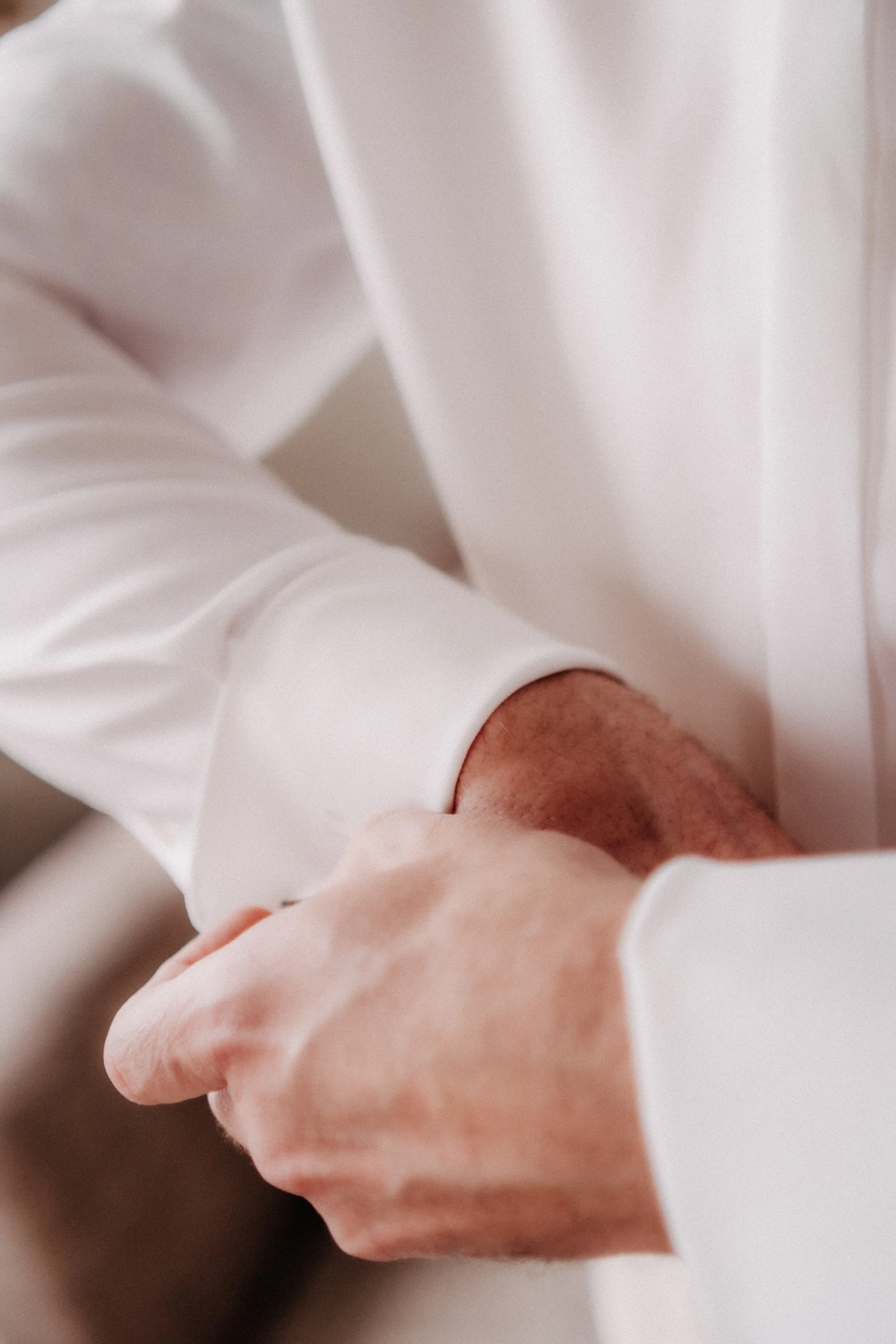 Nahaufnahme eines Mannes im weißen Hemd, der seine Armbanduhr an seinem Handgelenk anlegt.