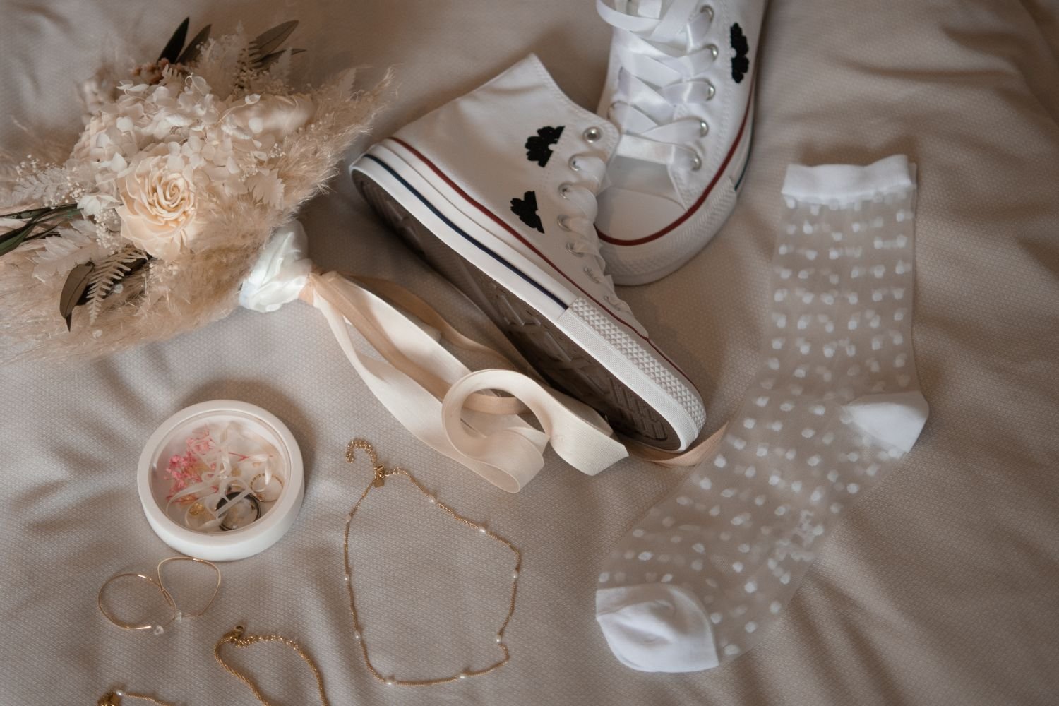 Blumenstrauß, weiße Turnschuhe, Socken, Schmuck und Kerze auf einem Bett.