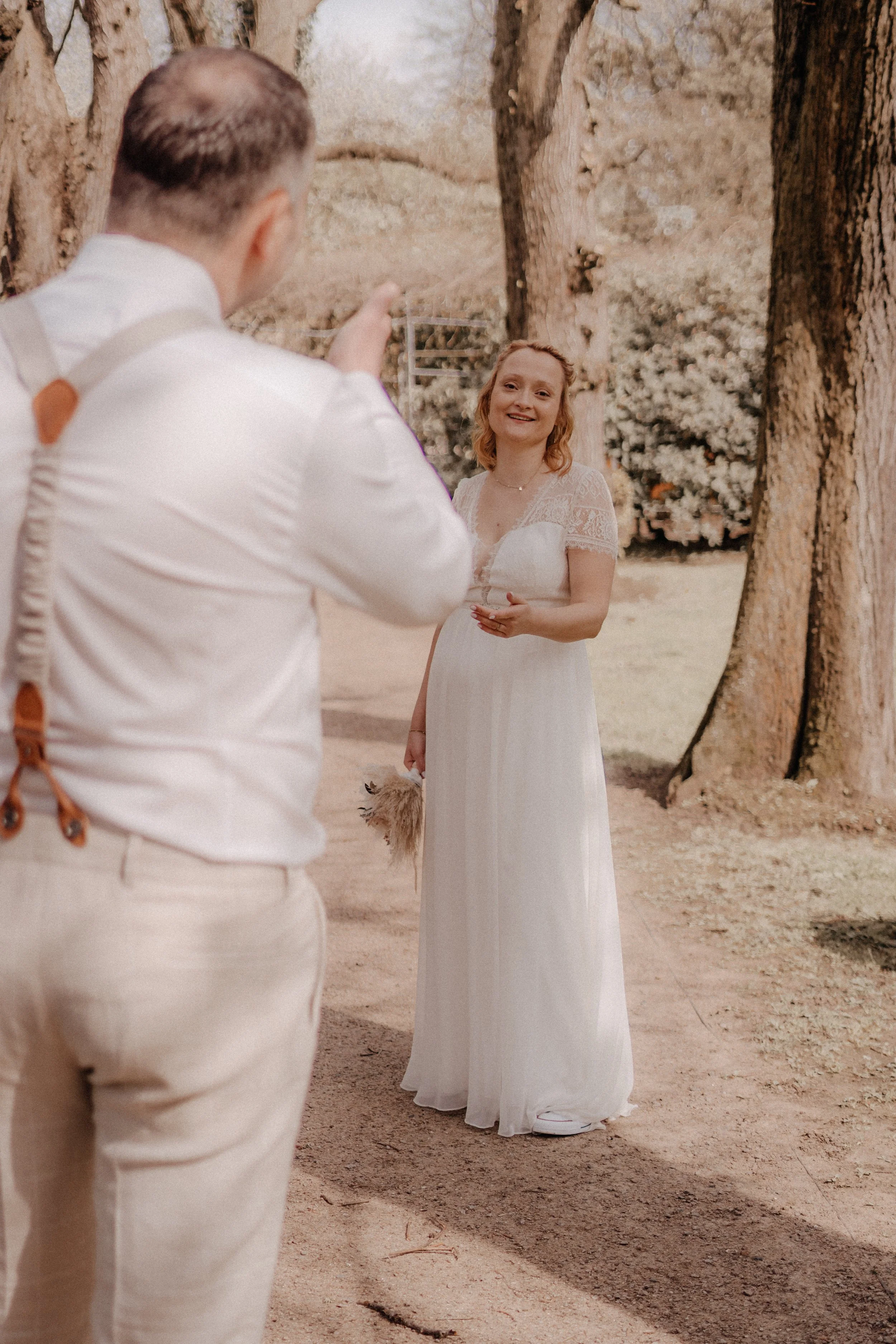 Braut im weißen Kleid lächelt während eines Fotoshootings im Freien, während der Fotograf im Vordergrund steht.