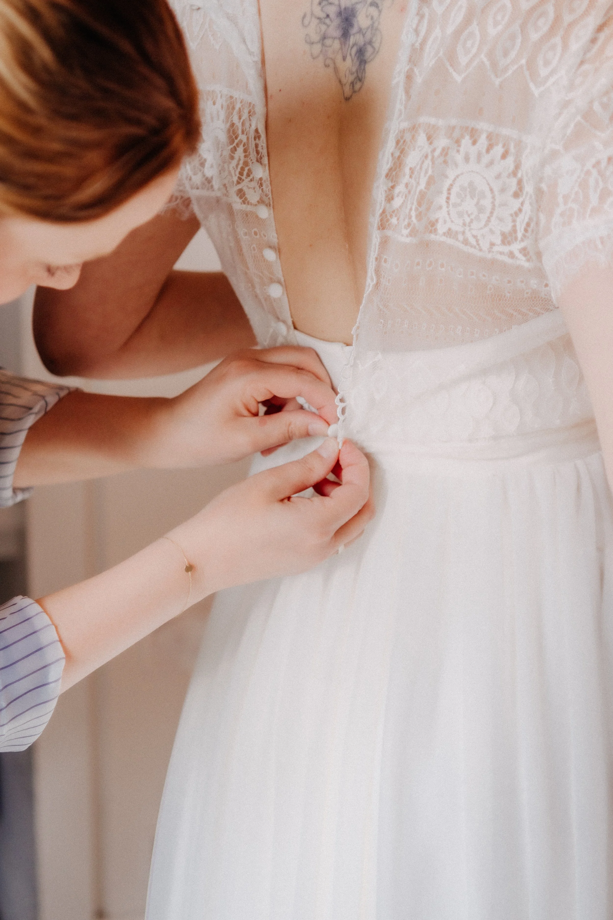 Die Knöpfe am Rücken des weißen Hochzeitskleids der Braut werden von der Schwester zugeknöpft.