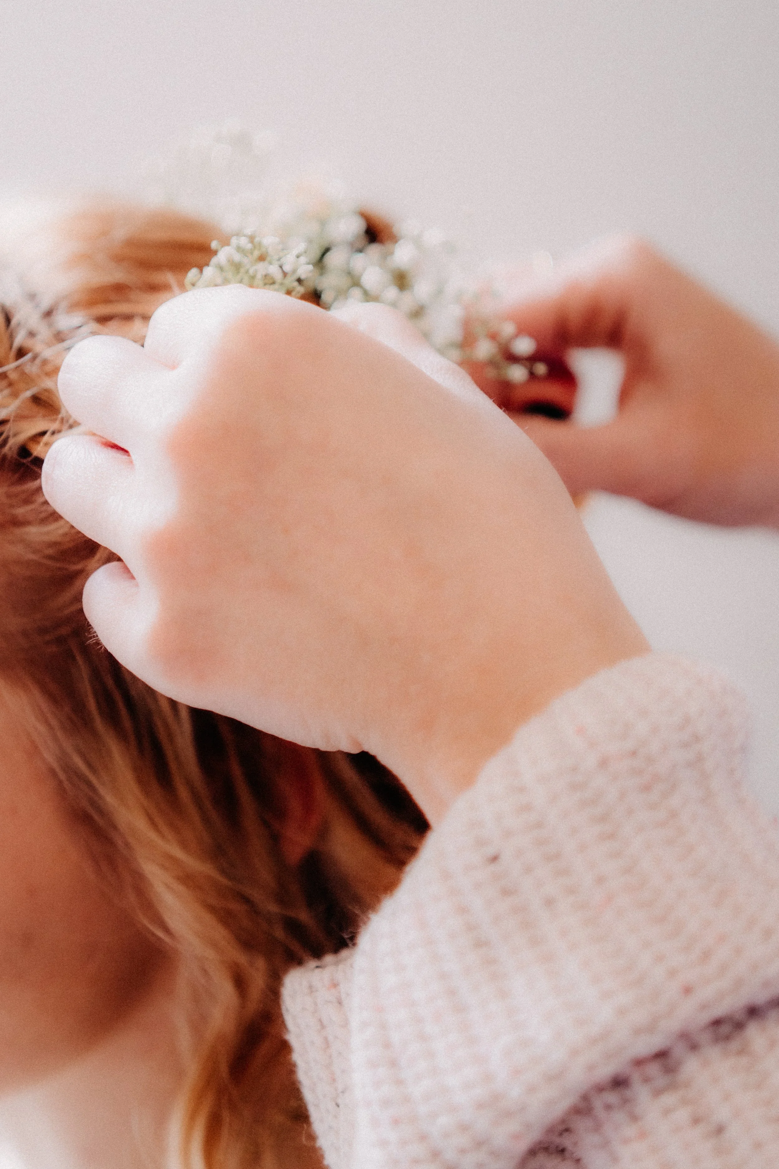 Person legt eine Hand aufs Haar, während sie eine kleine Blumenkrone trägt.