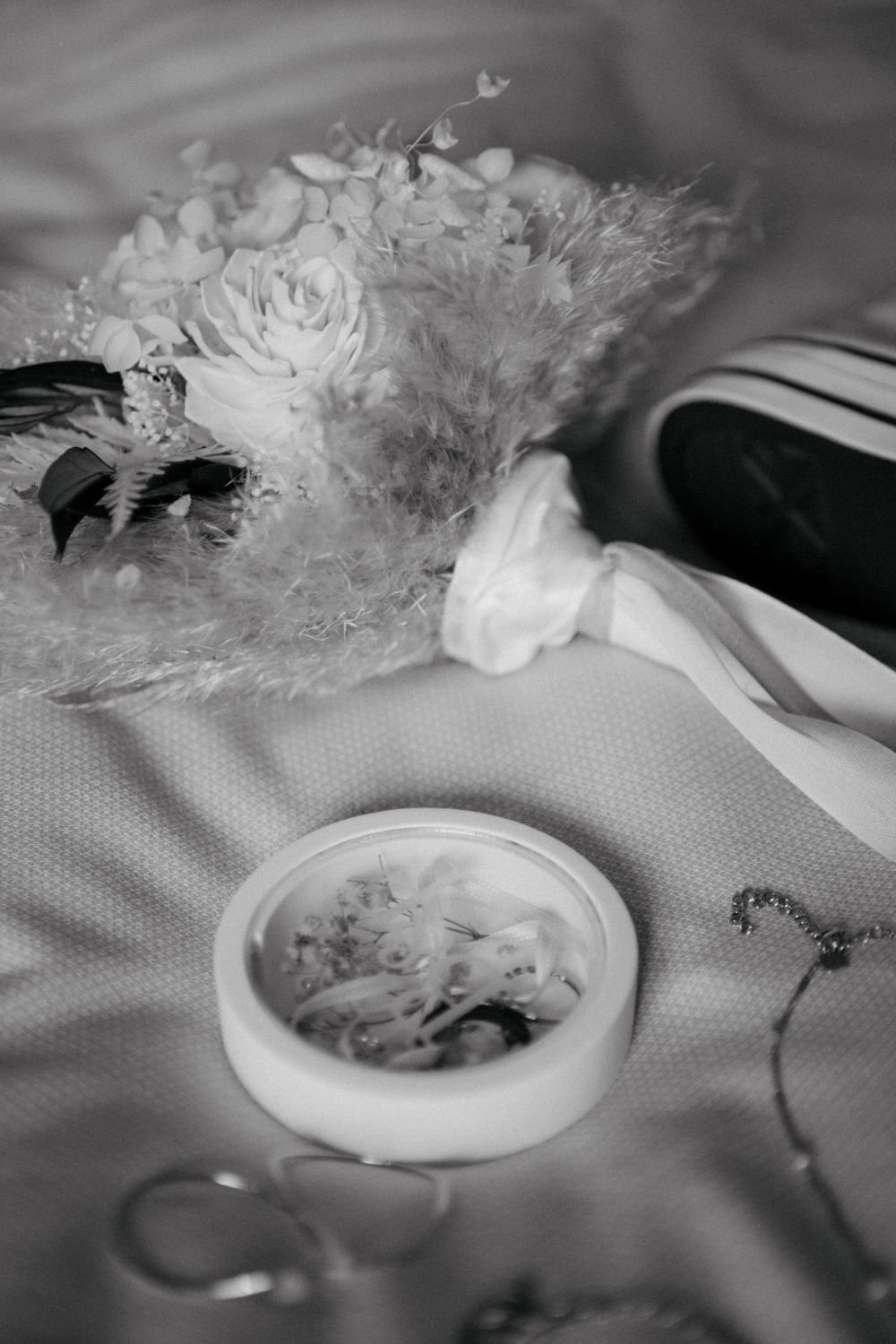 Blumengesteck auf einem Tisch, daneben ein Notenblatt in einer Schale, im Hintergrund Stoff und ein Teil eines Personenkleids.