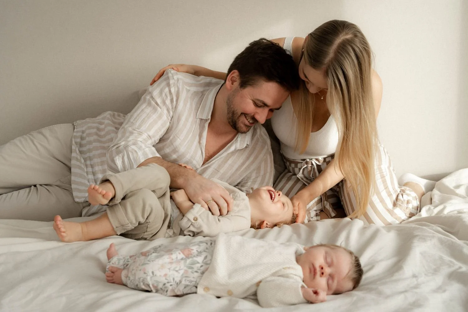 Familie spielt fröhlich auf dem Bett, zwei Kinder und zwei Erwachsene, nah beieinander, lachen, kuschliges Familienmoment.