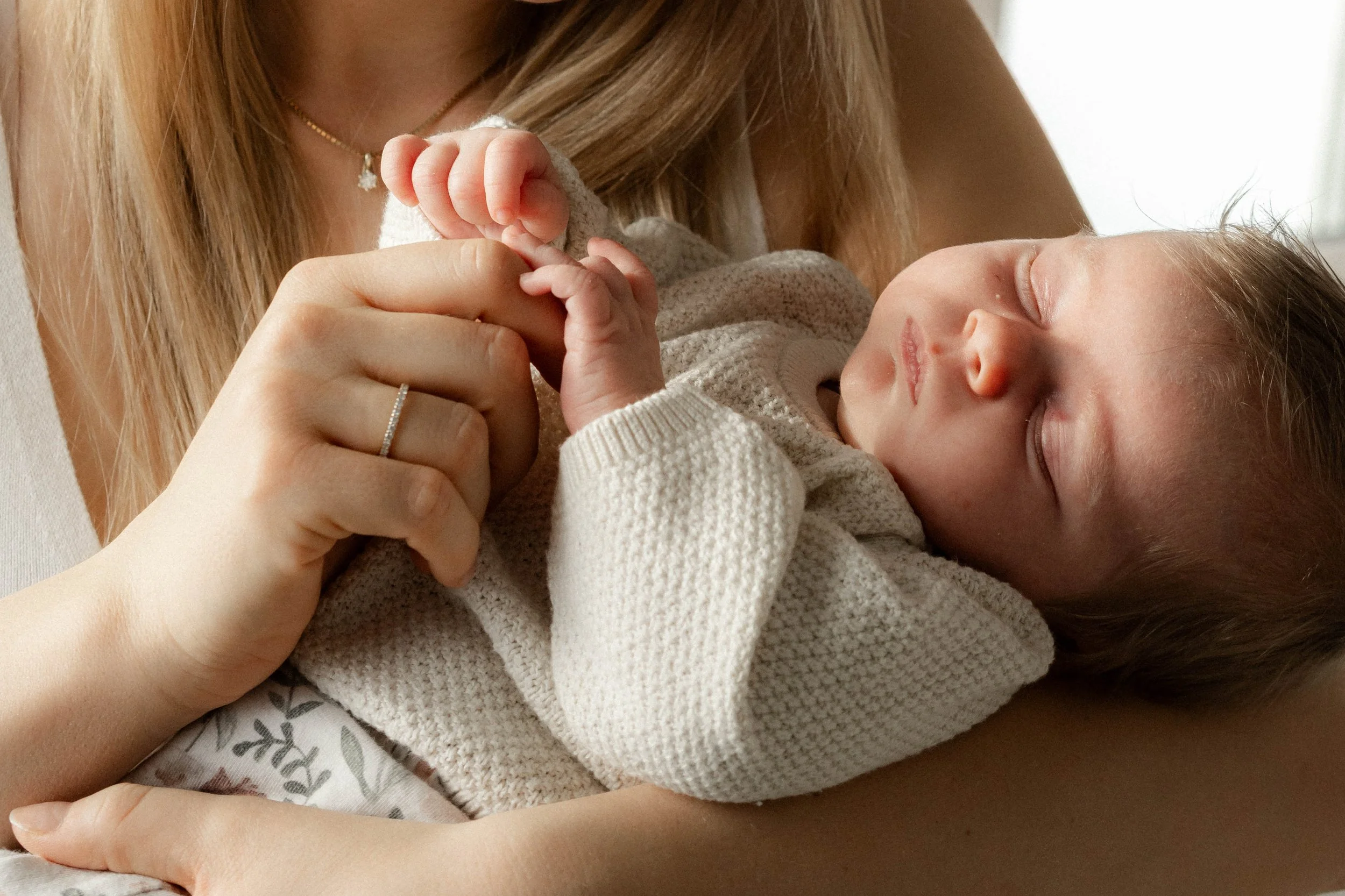 Eine Frau hält ein schlafendes Baby in den Armen, das einen weißen Pullover trägt.