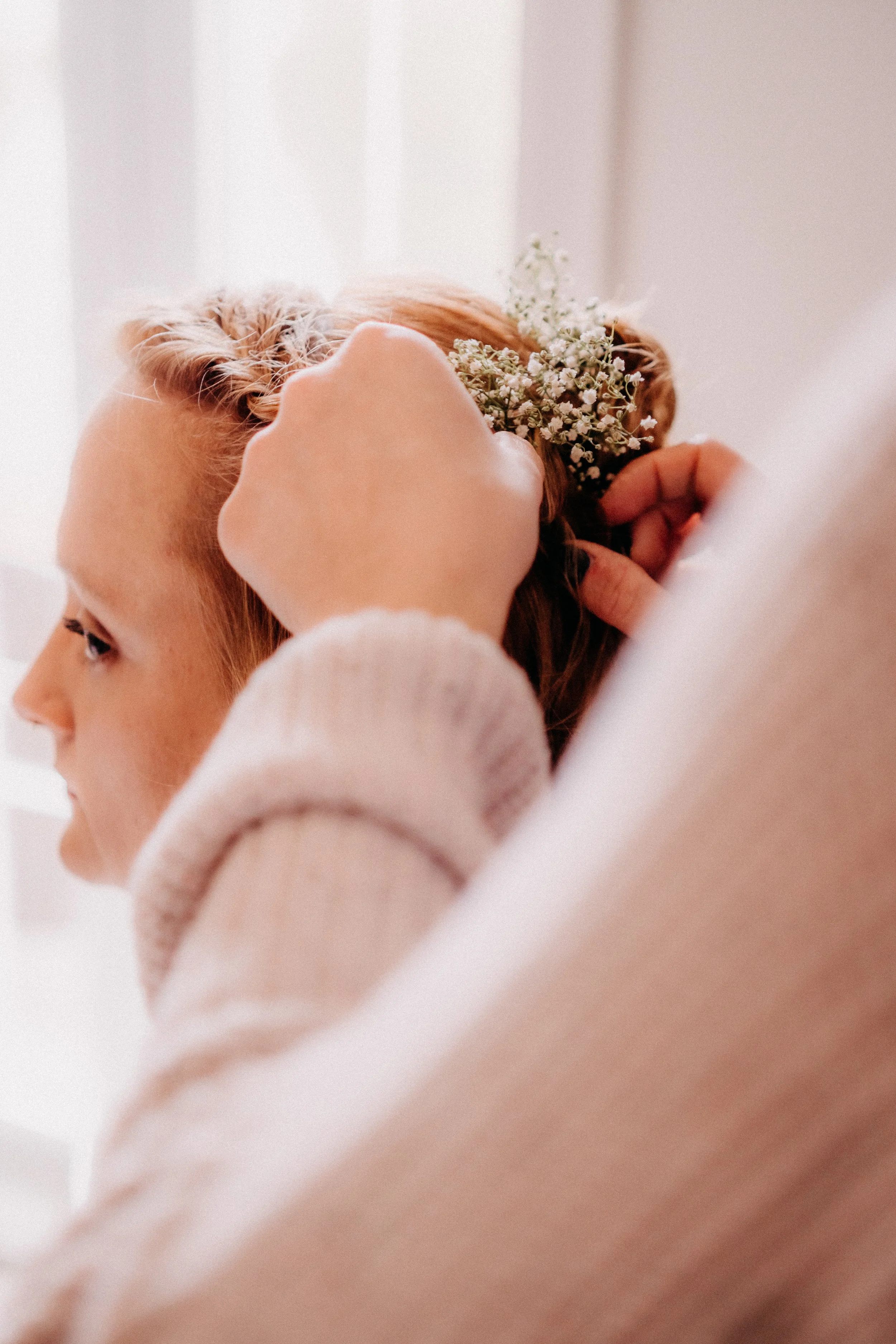 Eine Frau wird mit einer Blume am Ohr frisiert, während eine andere Person ihr dabei hilft, die Frisur zu gestalten.