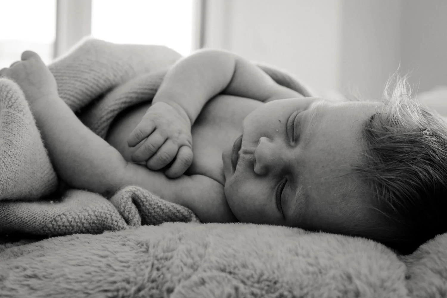 Schwarz-weiß-Foto eines schlafenden Babys, das auf einer weichen Decke liegt, mit geschlossenen Augen und einer Hand auf der Brust.