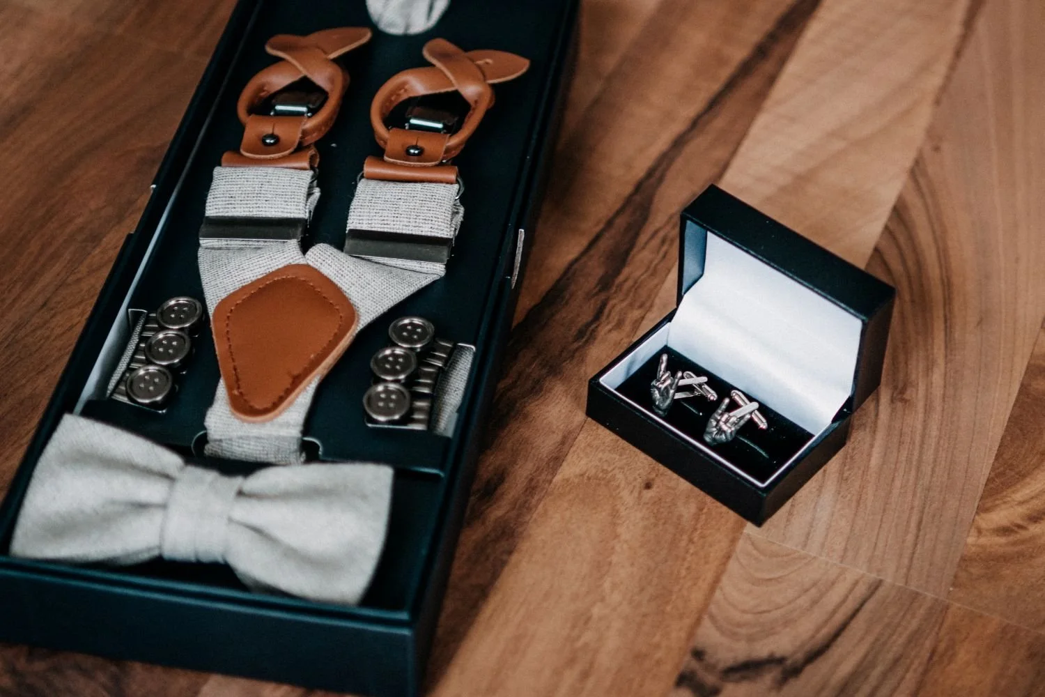 Herrenaccessoires auf Holztisch: Hosenträger im schwarzen Etui, Krawattennadel und Manschettenknöpfe in einer schwarzen Box mit Spiegel