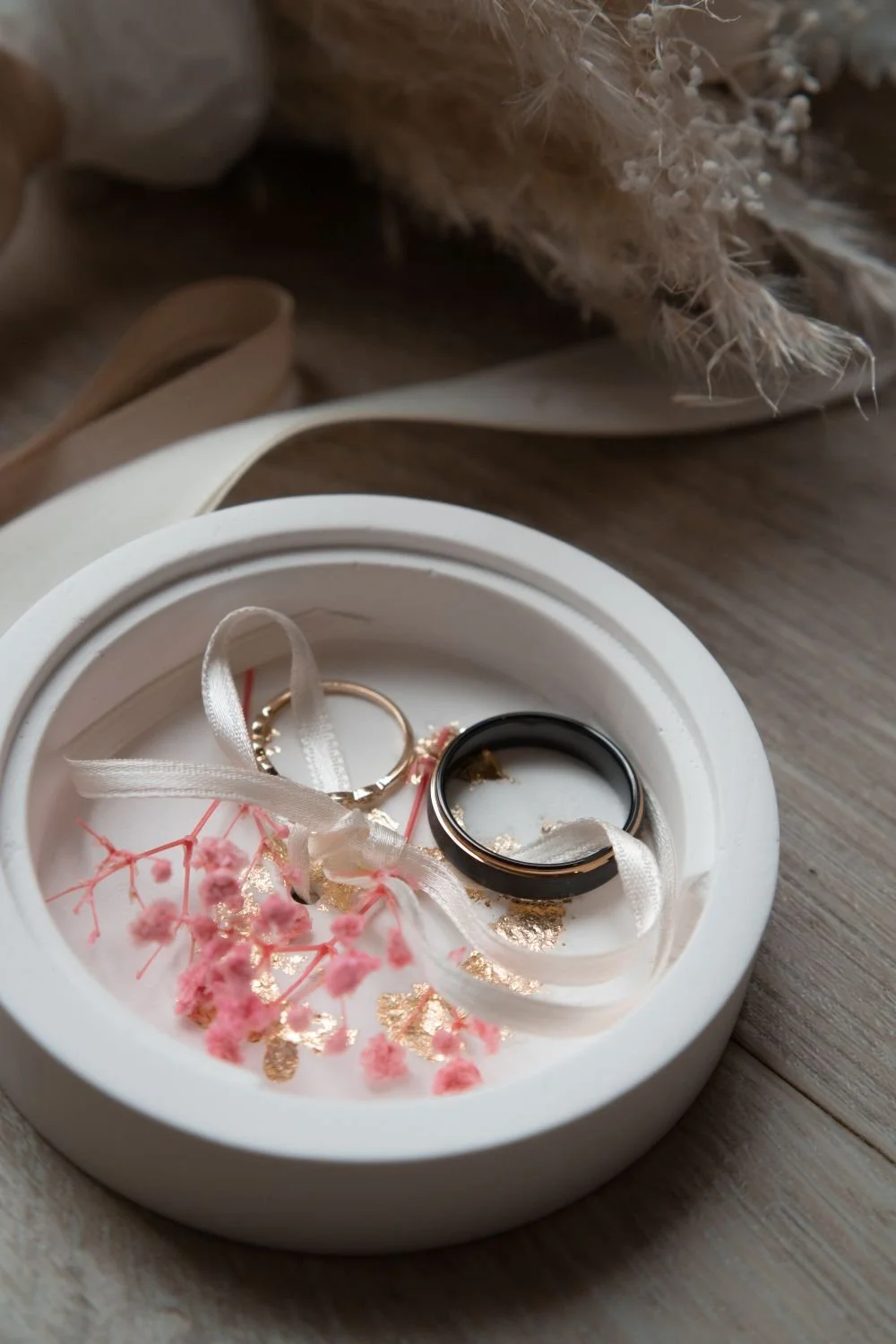 Schlichte weiße Ringbox mit zwei Eheringen und rosa Trockenblumen