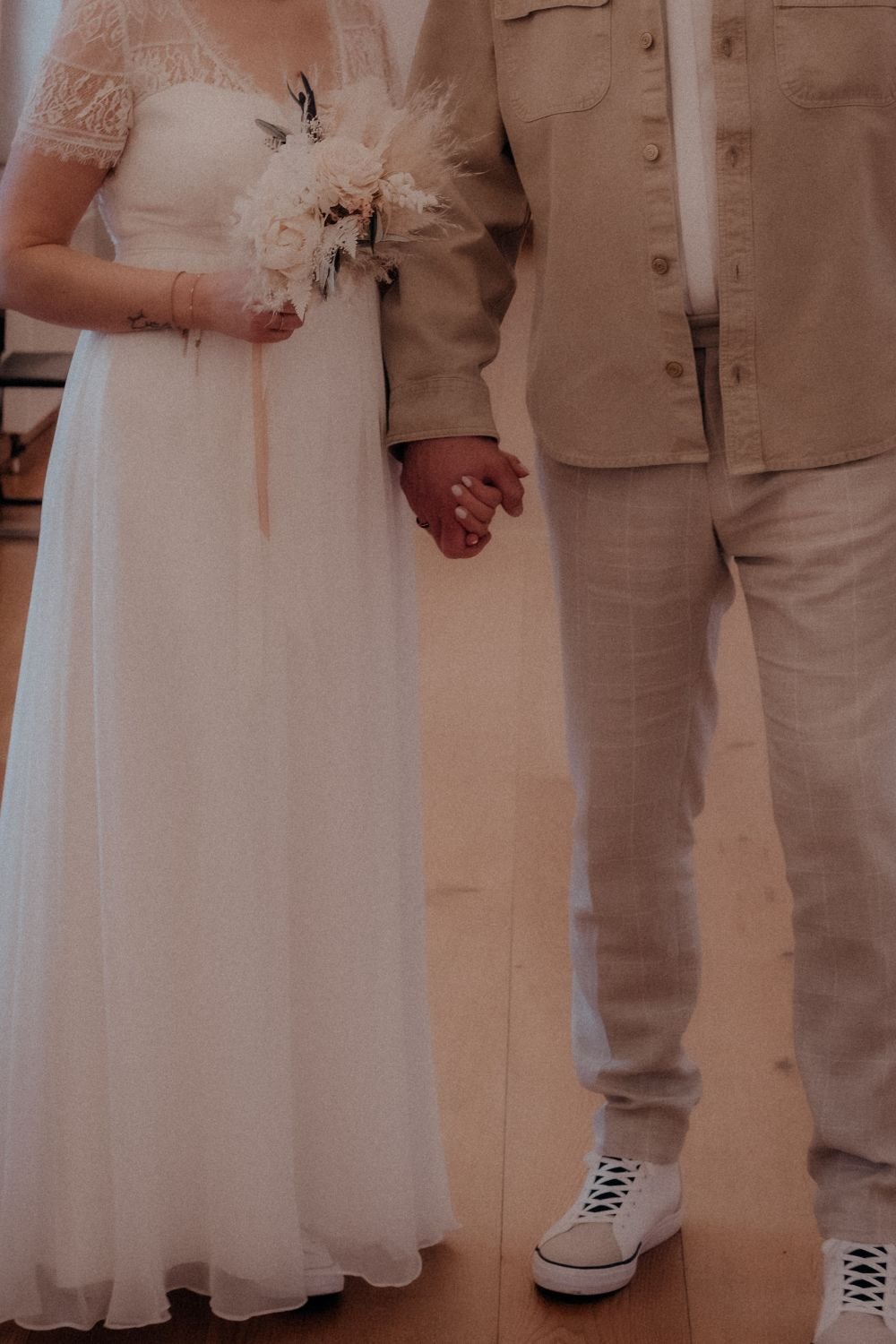 Ein Brautpaar hält sich an den Händen und trägt helle, elegante Kleidung während einer Zeremonie.