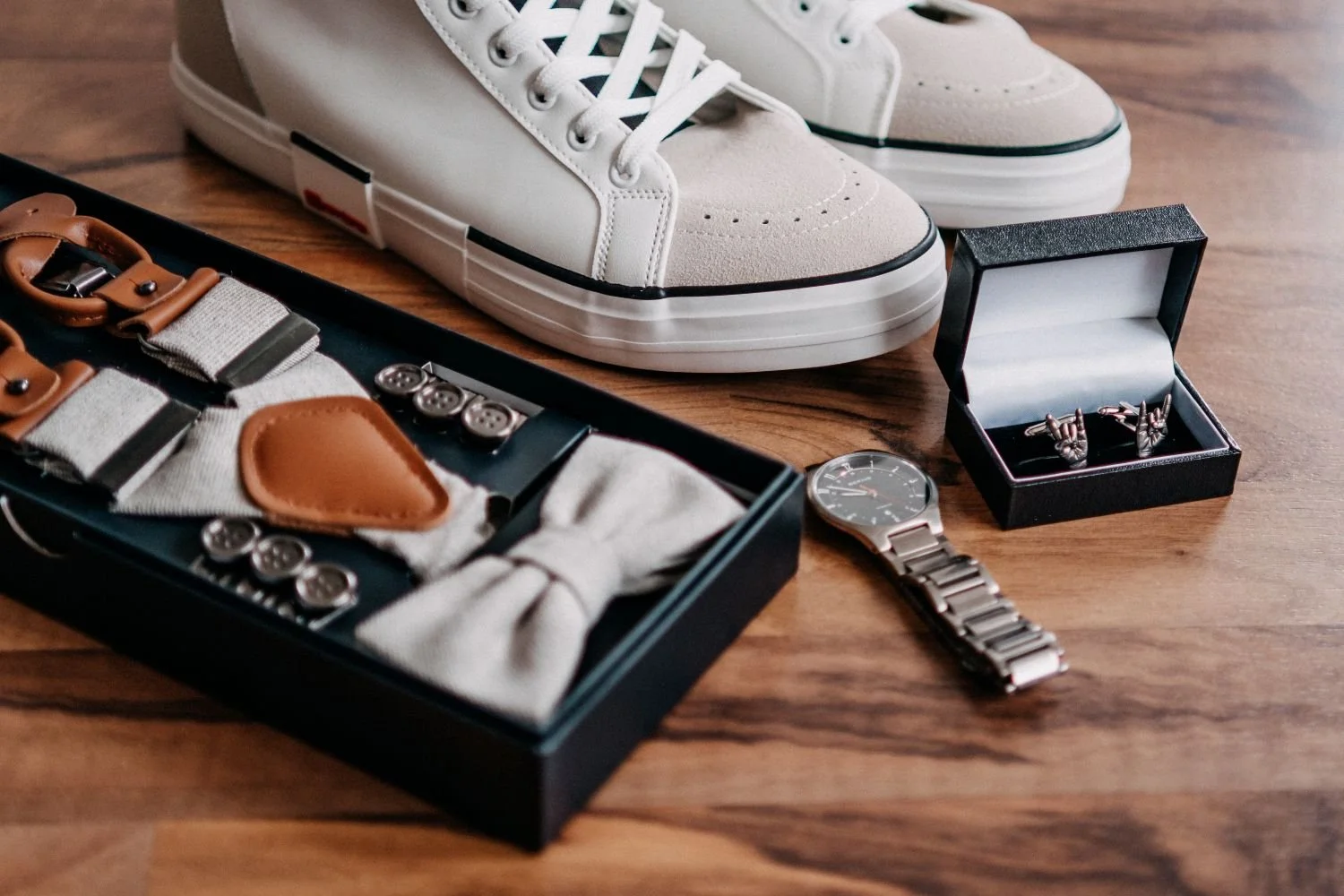 Weiße Sneakers, Armbanduhr, Manschettenknöpfe in einer Geschenkbox, Schnürbänder und Hosenträger auf einem Holztisch