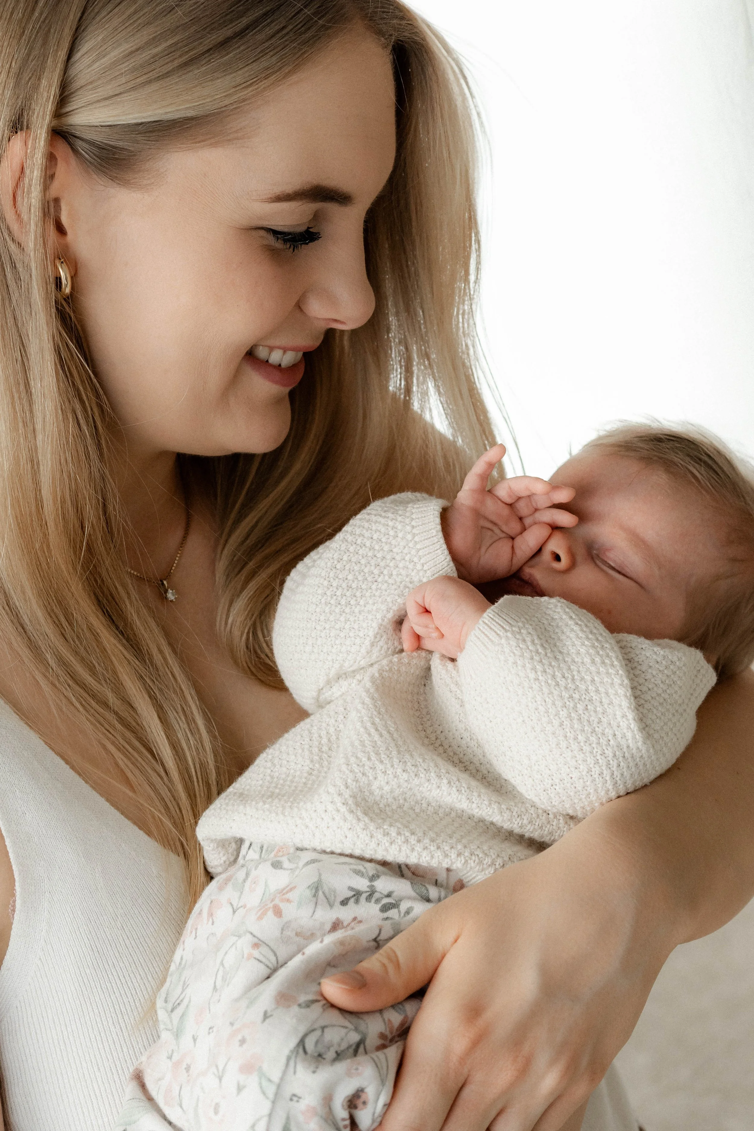 Eine Frau hält ein schlafendes Baby in ihren Armen, beide lächeln sich an.