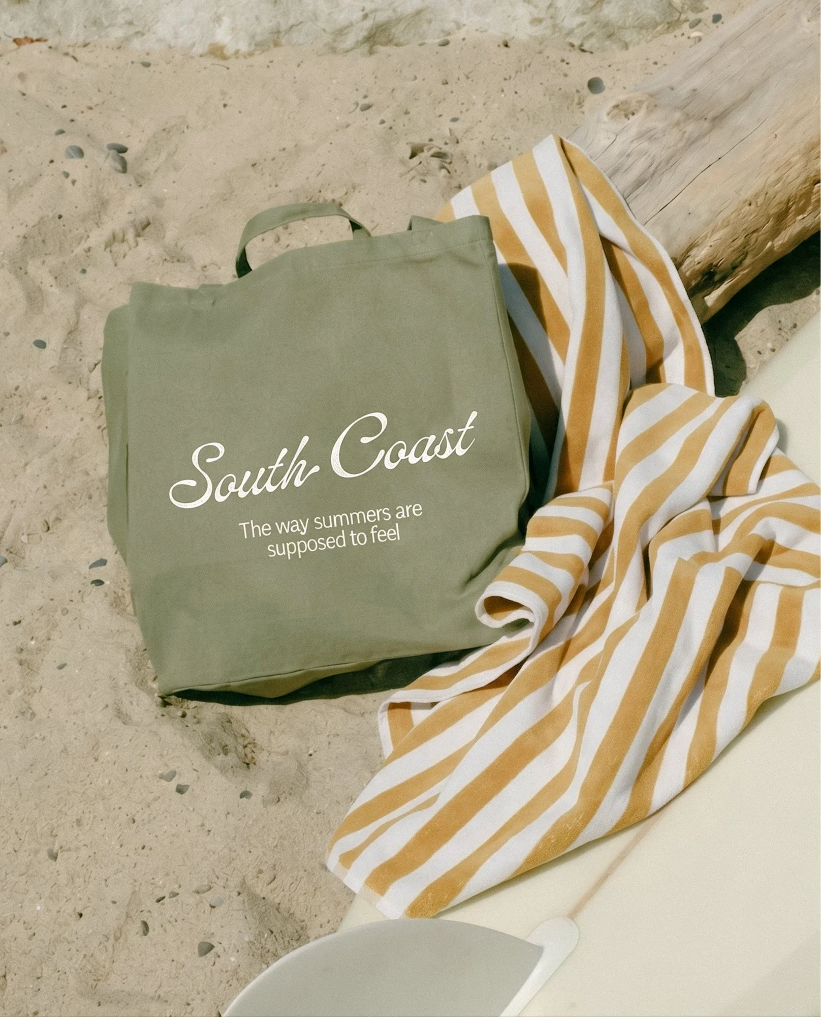 Branded tote bag mockup on the beach with surfboard — lifestyle brand identity design for South Coast Swimwear