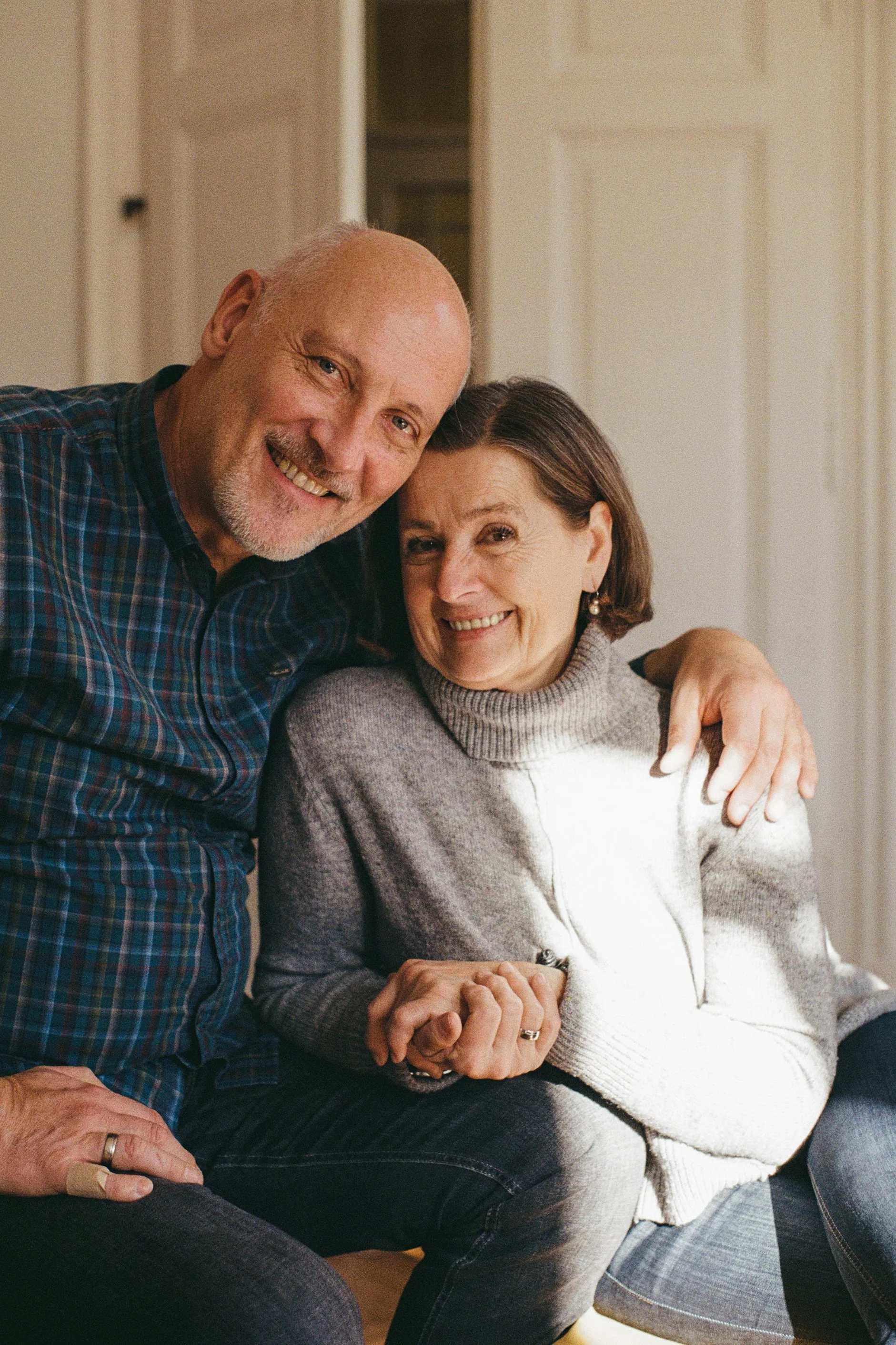 A happy elderly man and woman sitting close together, smiling at the camera, with the man placing his arm around the woman.