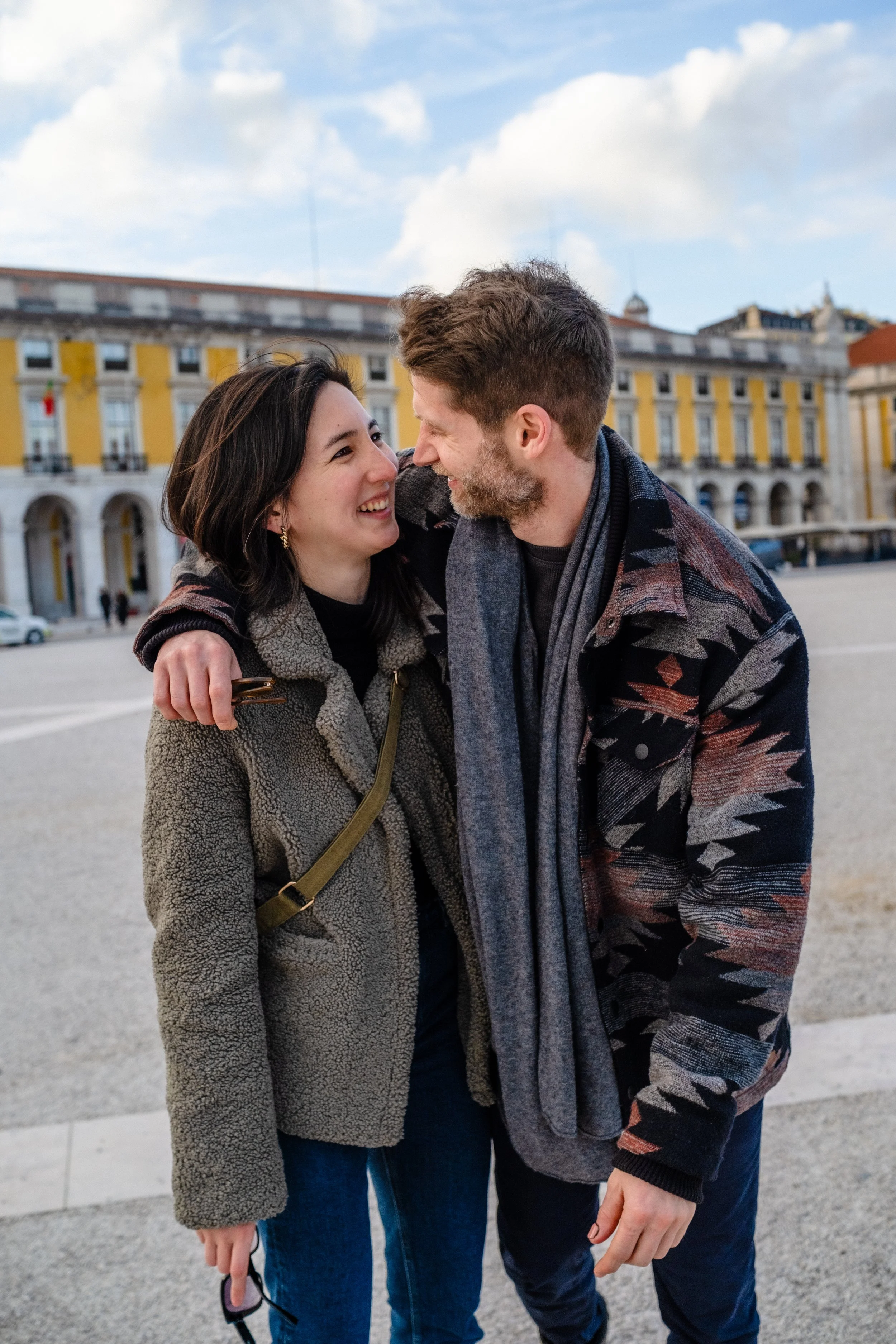 A man and woman smiling at each other and embracing in a city square during the day.