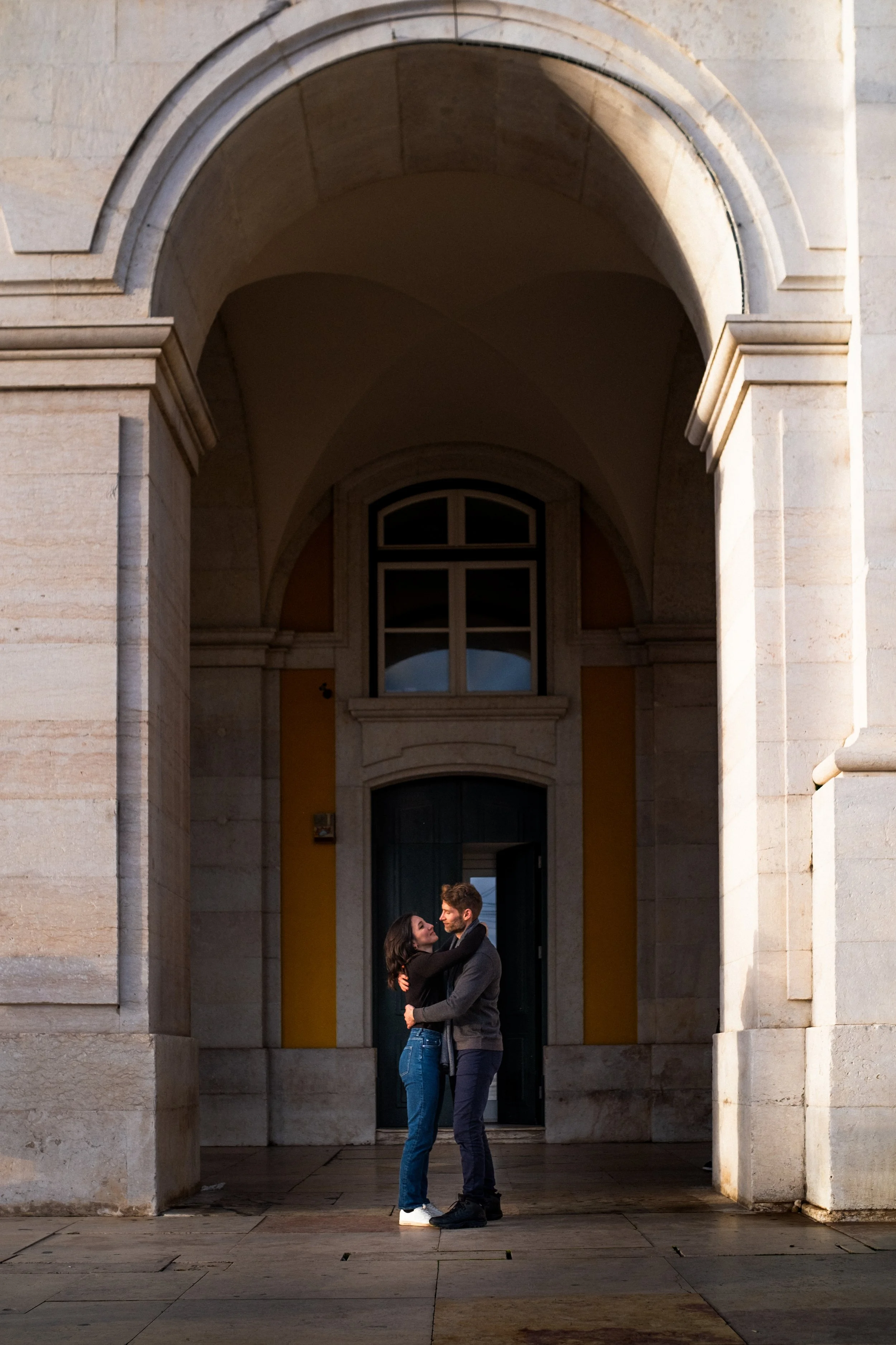A couple embracing under an archway in front of a historic building.