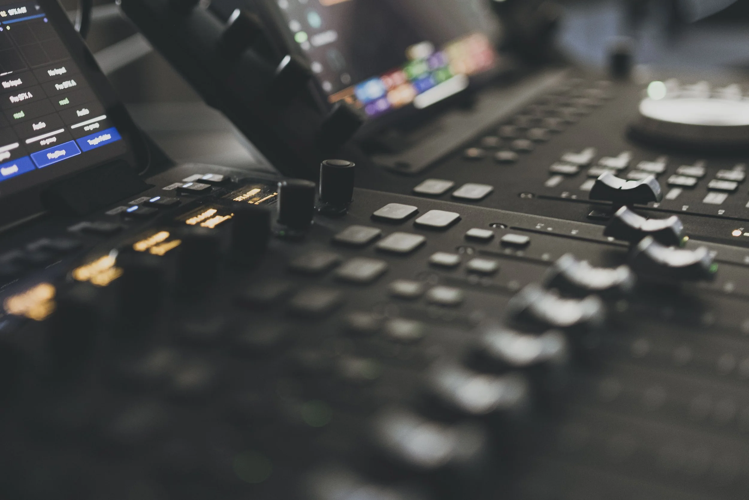 Close-up of a professional audio mixing console with various faders, knobs, and a digital screen displaying colorful audio levels.