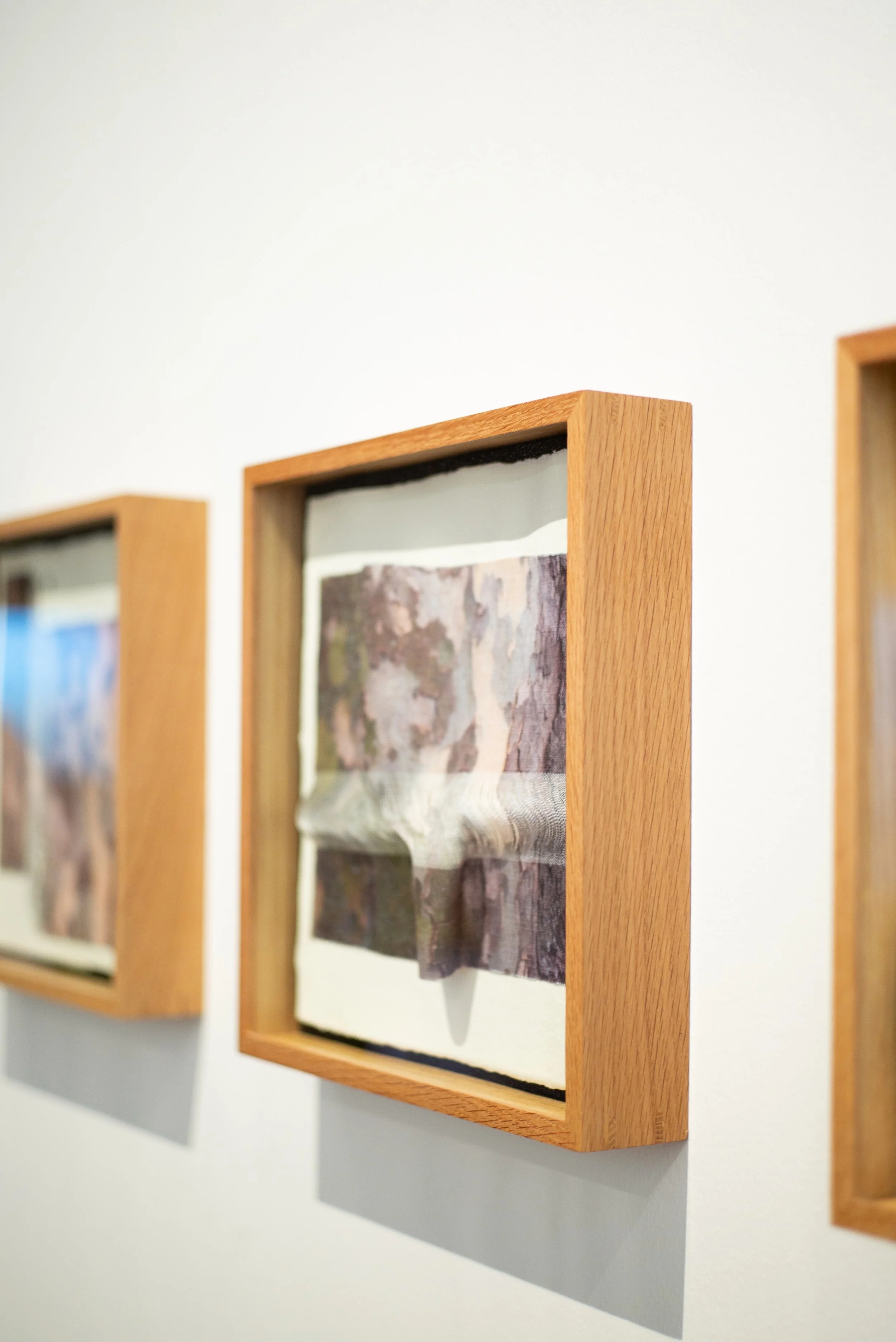 Framed artwork with layered fabric and paint textures on a white wall.