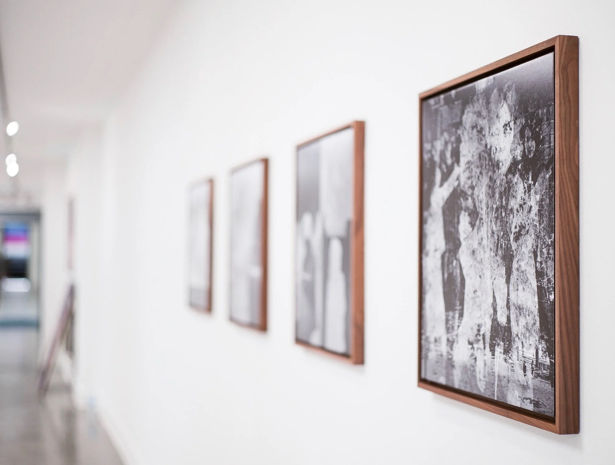 Black and white photos framed in wood hang on a white gallery wall, blurred at the far end of the corridor.