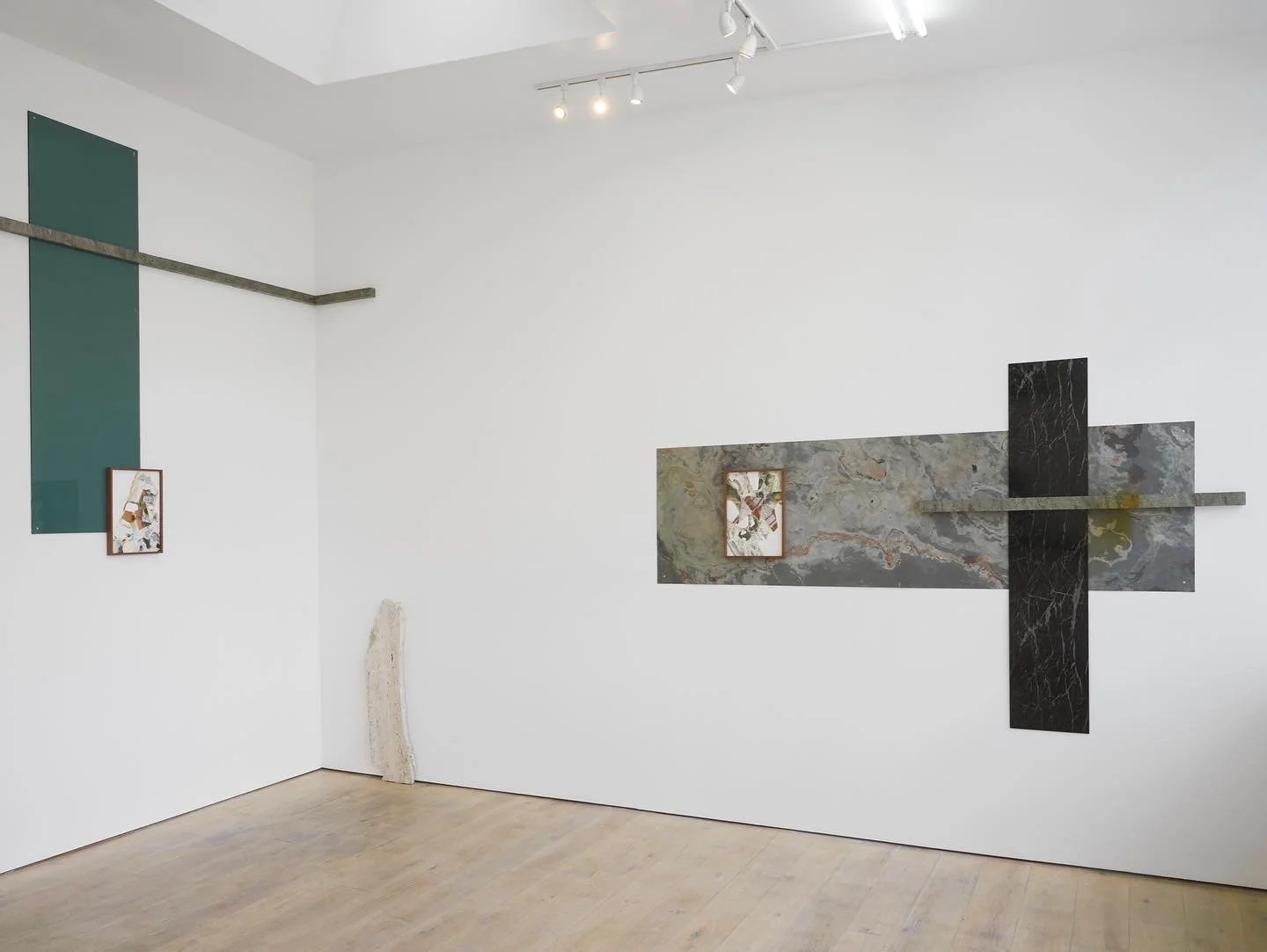 Art installation on a white gallery wall featuring rectangular marble panels with suspended smaller framed artworks.