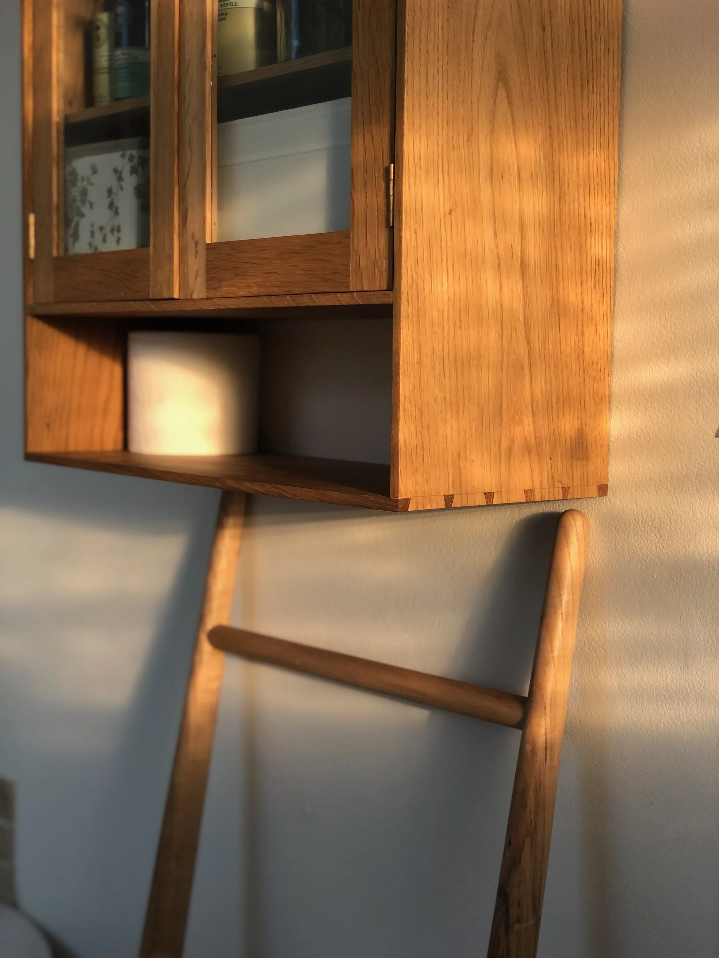 Wooden cabinet with glass-paneled doors mounted on a light-colored wall, with a wooden towel rail beneath it.