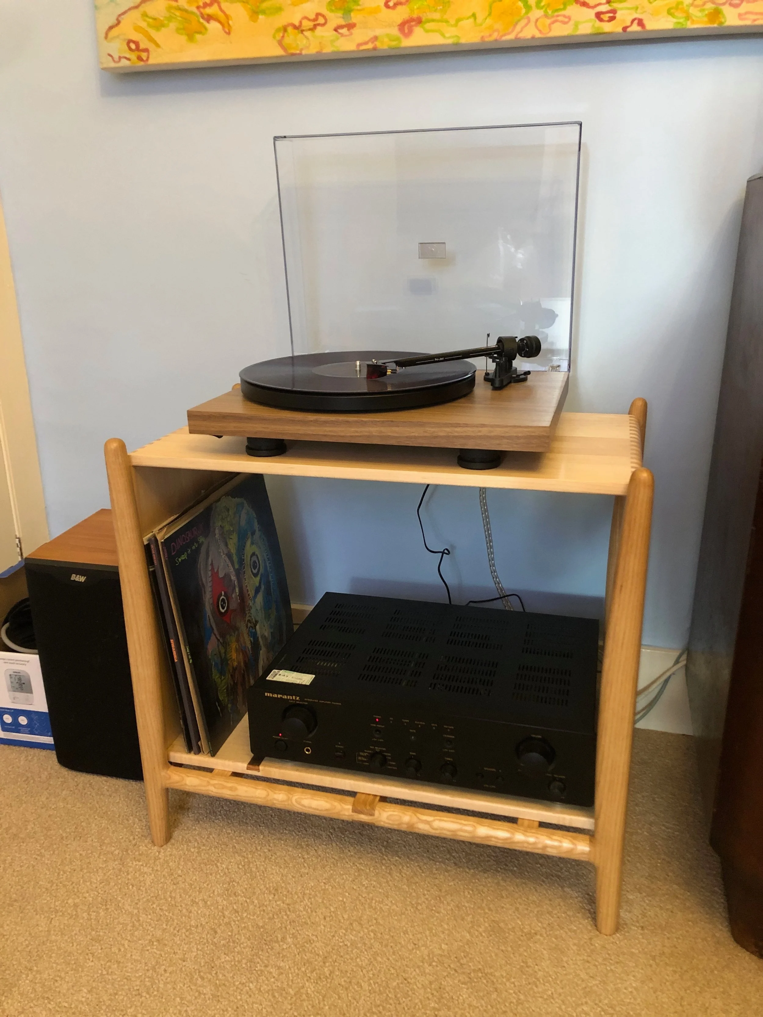 A turntable on a wooden stand and an amplifier with vinyl records leaning against it underneath.