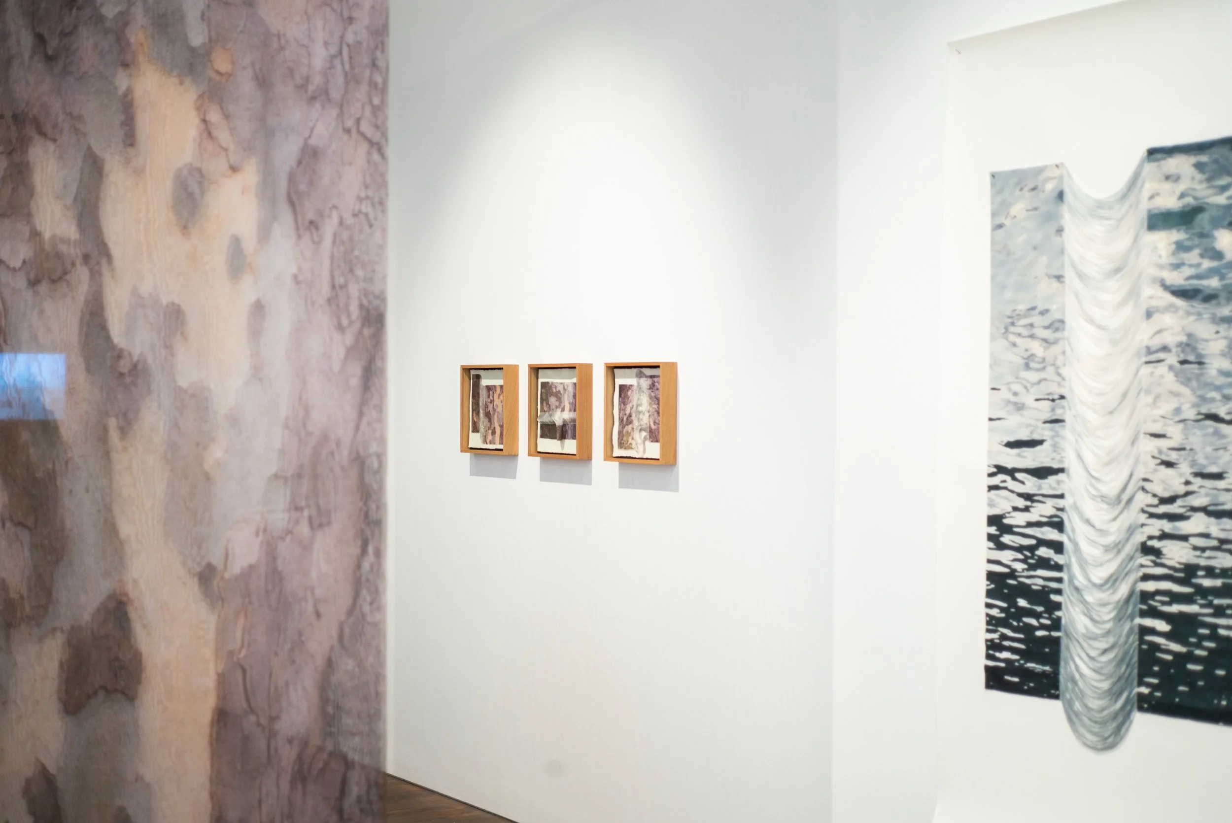Gallery wall with three small framed abstract artworks on a white wall, and a larger abstract painting with a water-themed design beside them.