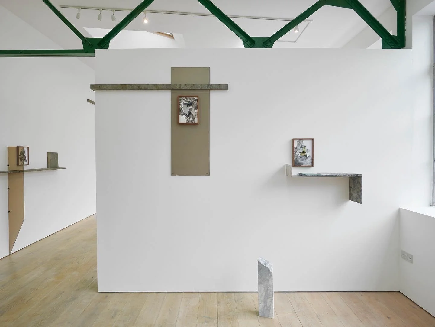 Minimalist art gallery with white walls, wooden floors, green ceiling beams, and suspended abstract paintings and objects.