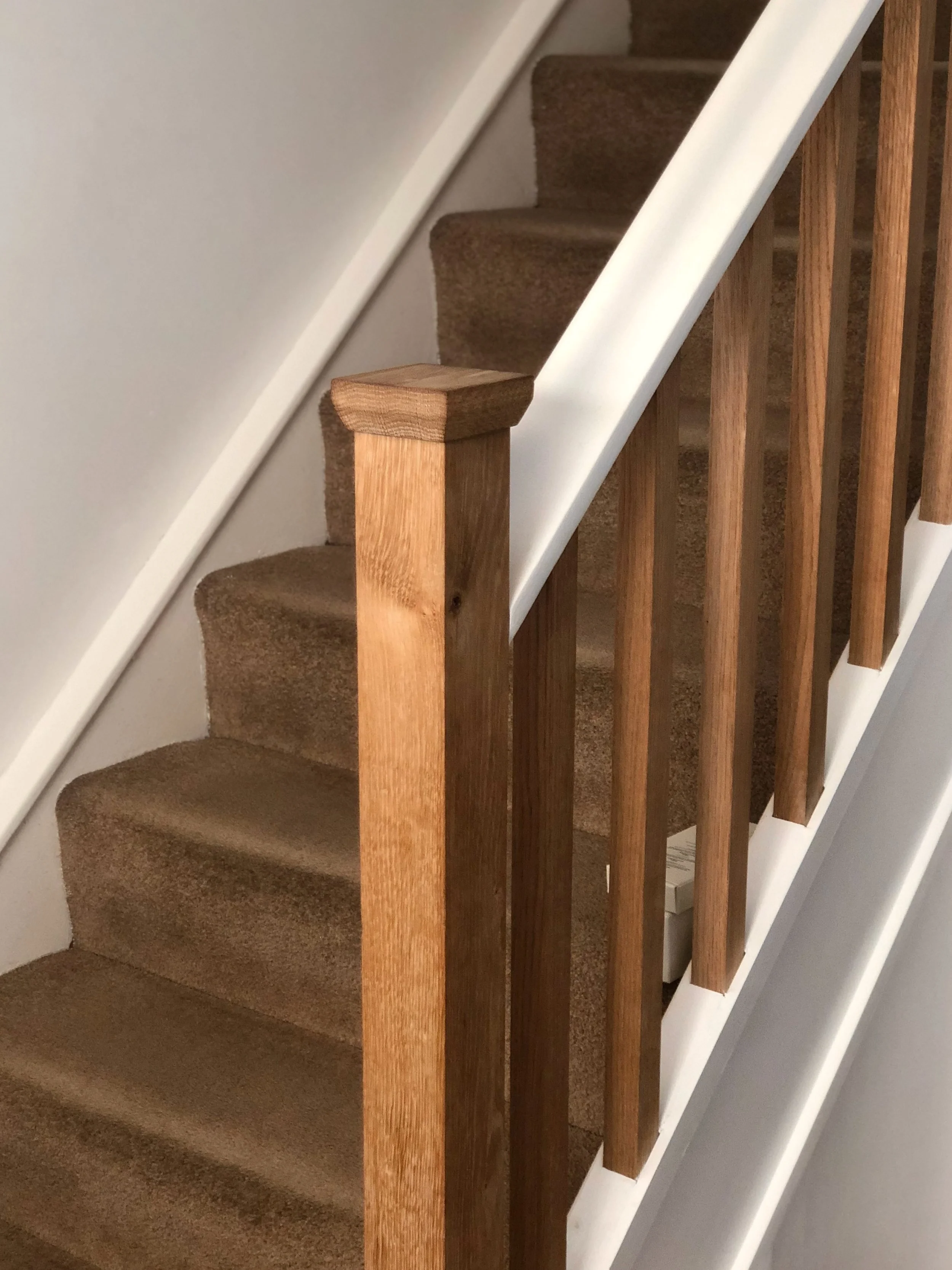 A staircase with brown carpeted steps, a wooden handrail, and wooden balusters.