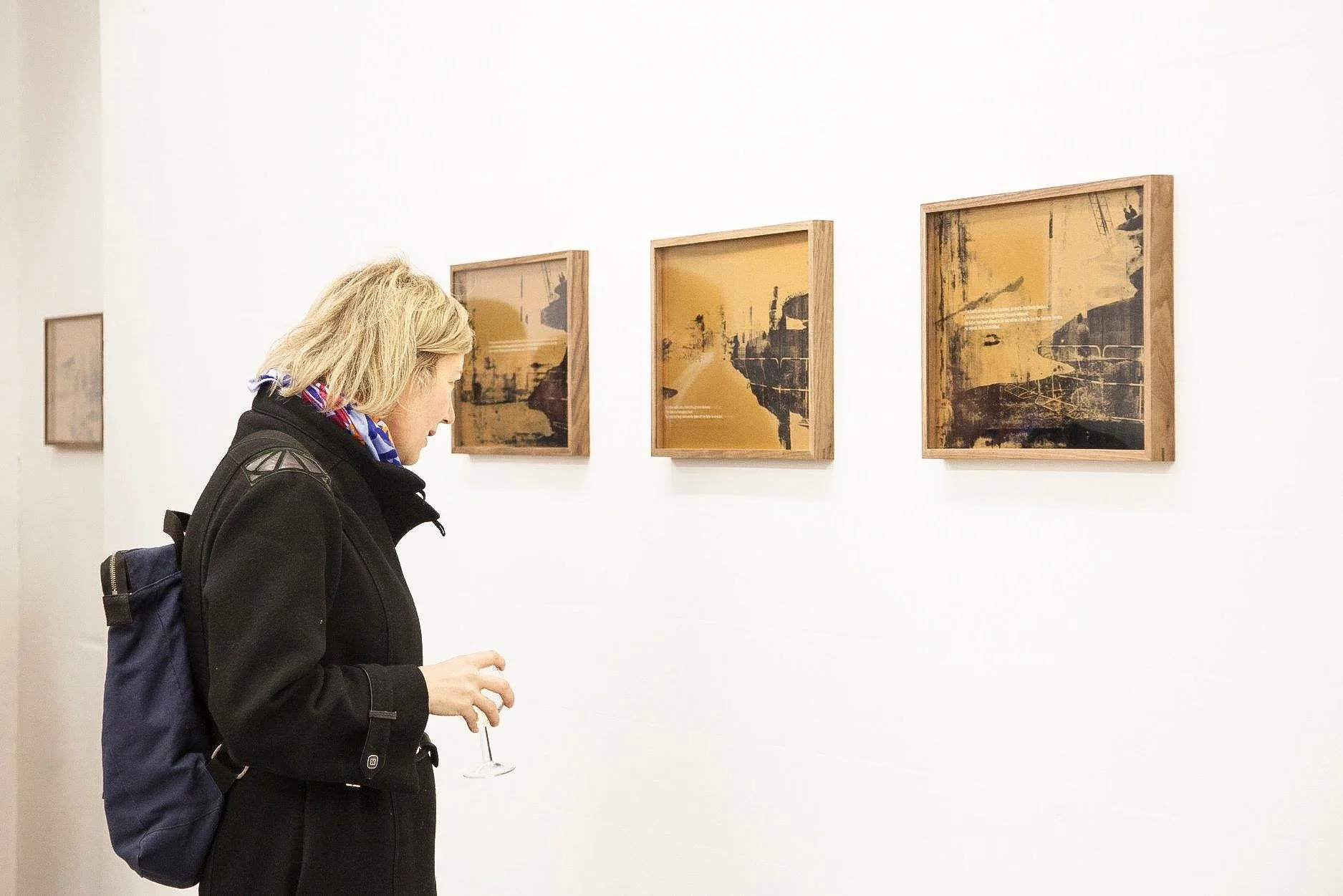 A woman viewing abstract artwork in a gallery, holding a glass of wine.
