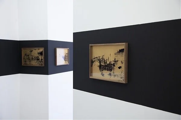 Three abstract paintings mounted on a wall that is painted half black and half white.