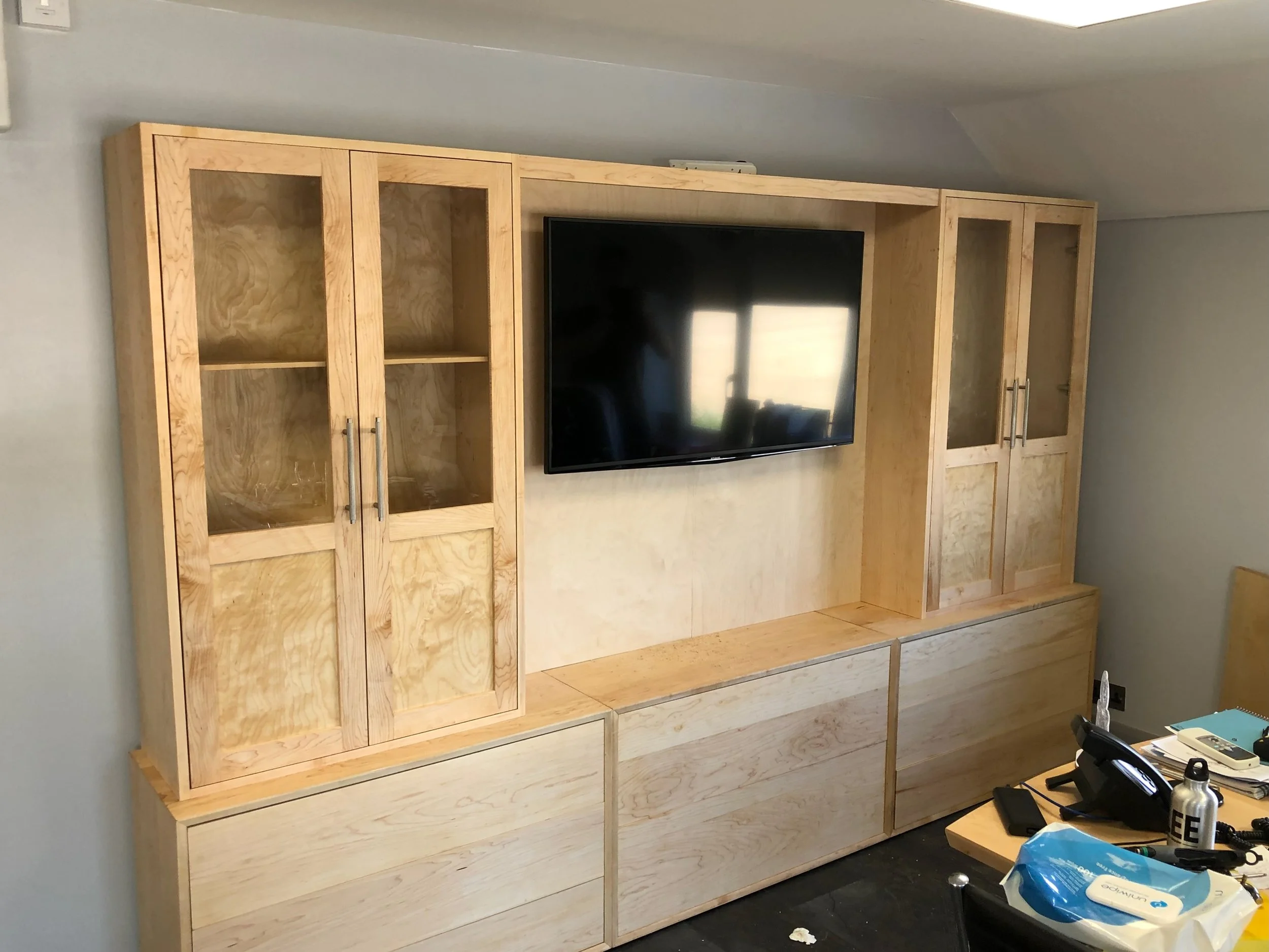 A wooden entertainment center with cabinets and drawers, mounted on a white wall, with a flat-screen TV in the center.