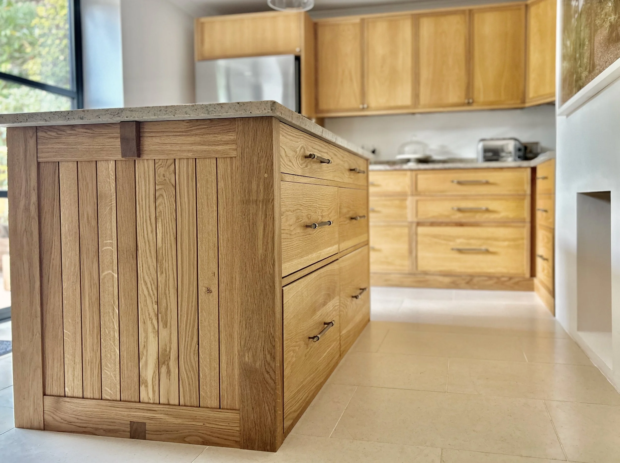 Wooden kitchen island with a marble top in a modern kitchen with wooden cabinets and appliances in the background.