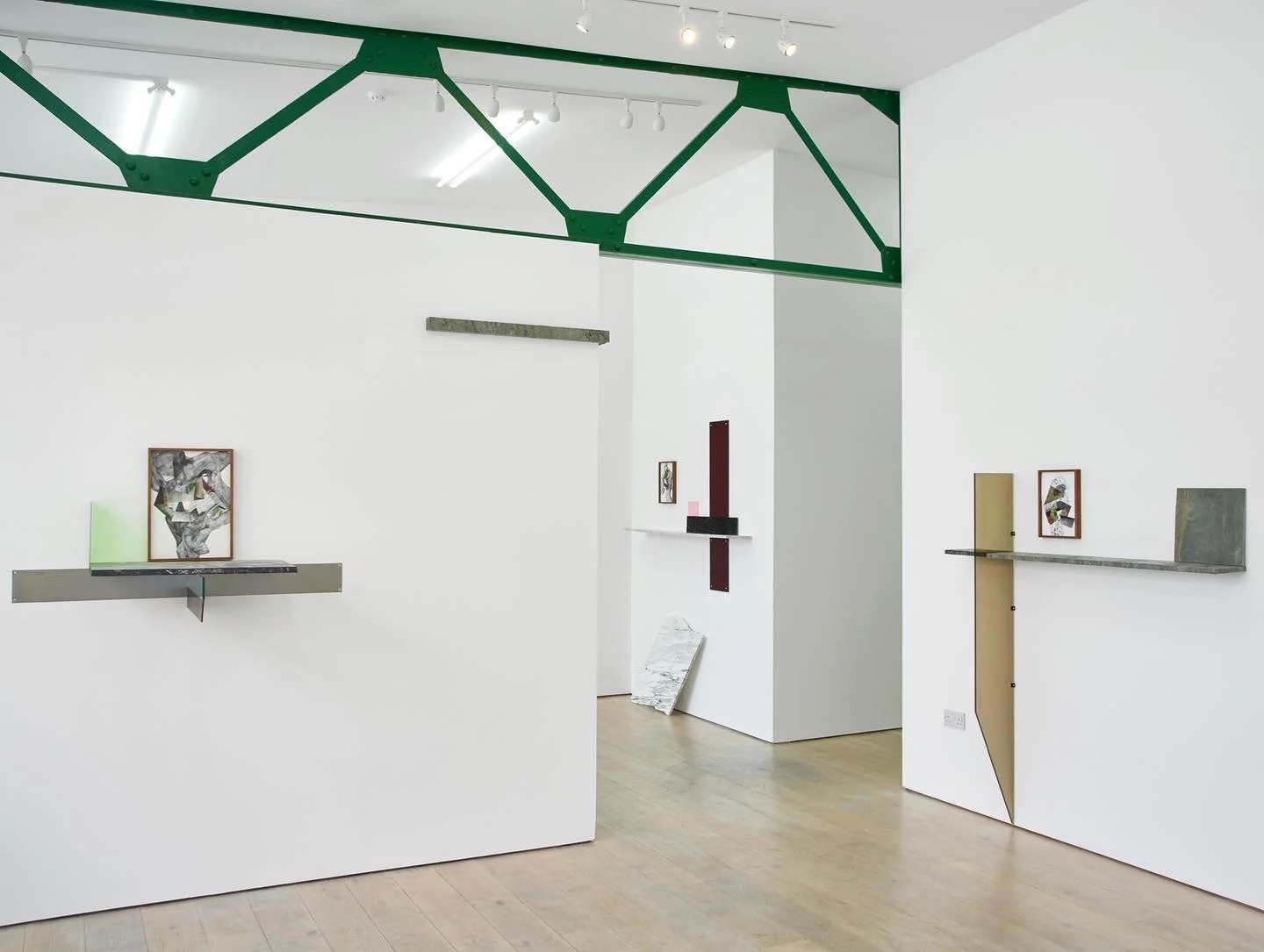 Modern art gallery with white walls, wood floors, and minimalist sculptures and framed artworks displayed on floating shelves.