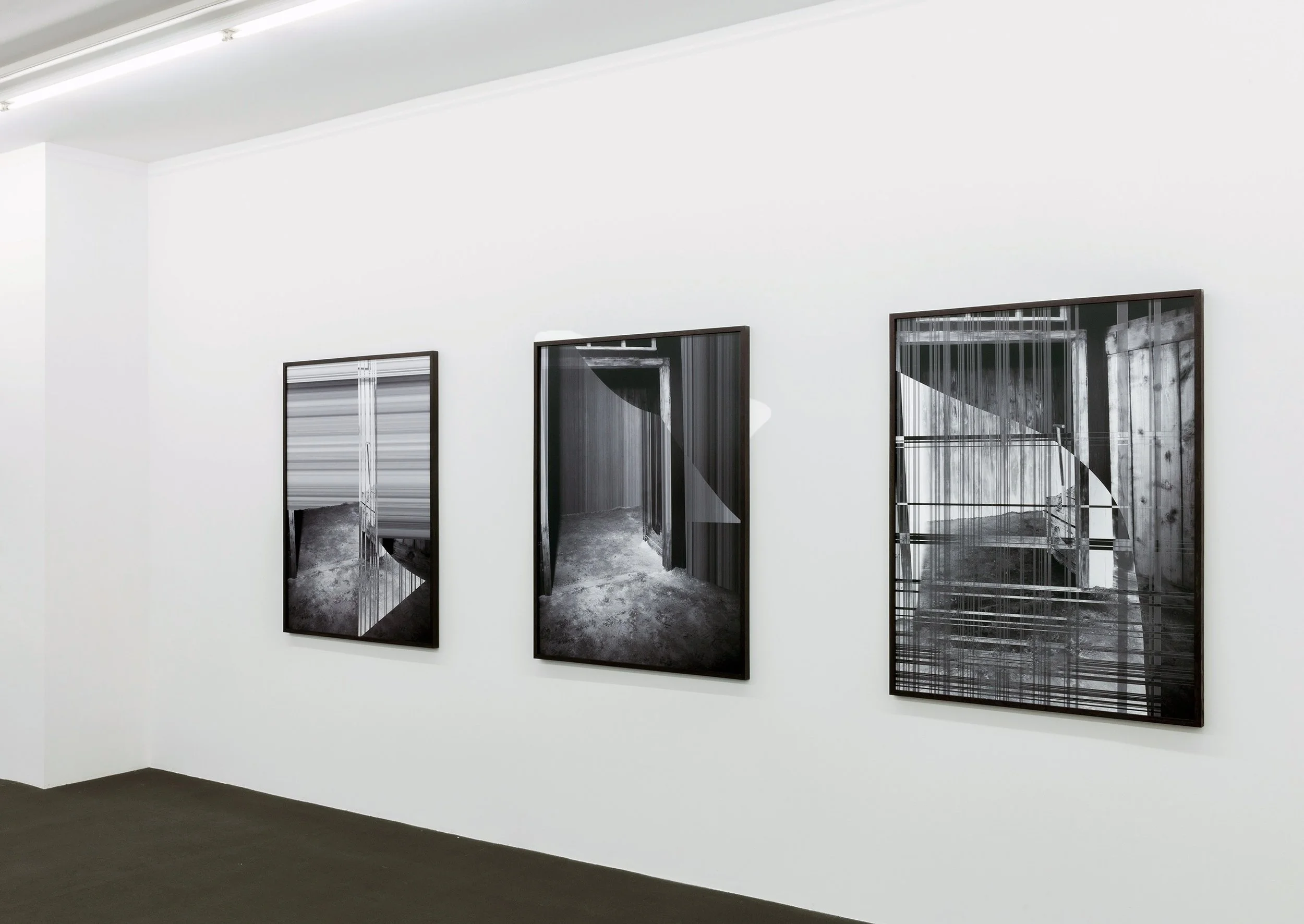 Black and white photographs on gallery wall showing doorways and structural elements, featuring abstract architectural patterns.