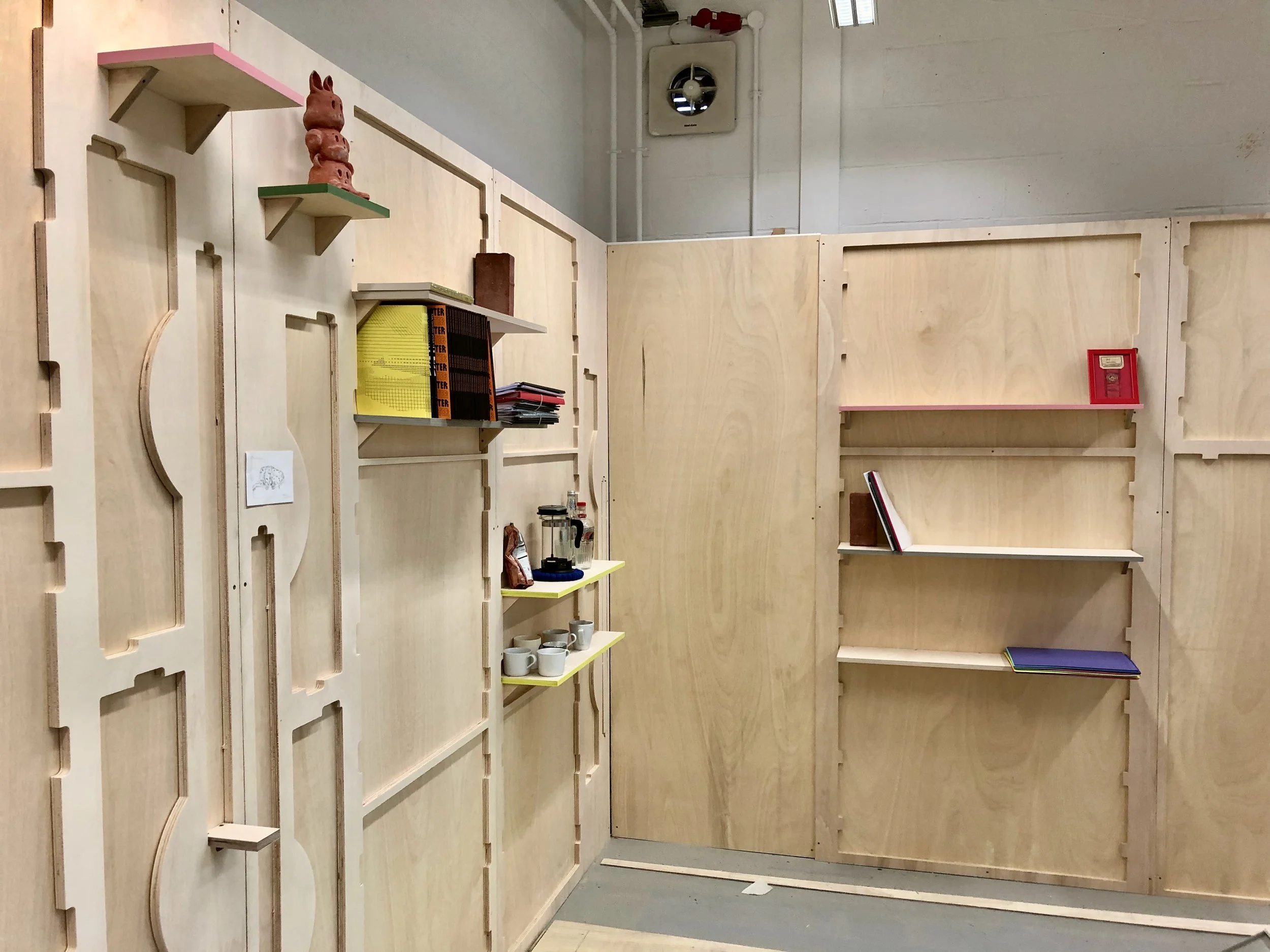 Interior of a room with light-colored wooden shelves and wall panels, some decorated with various small items, including books, a small red box, and cups.