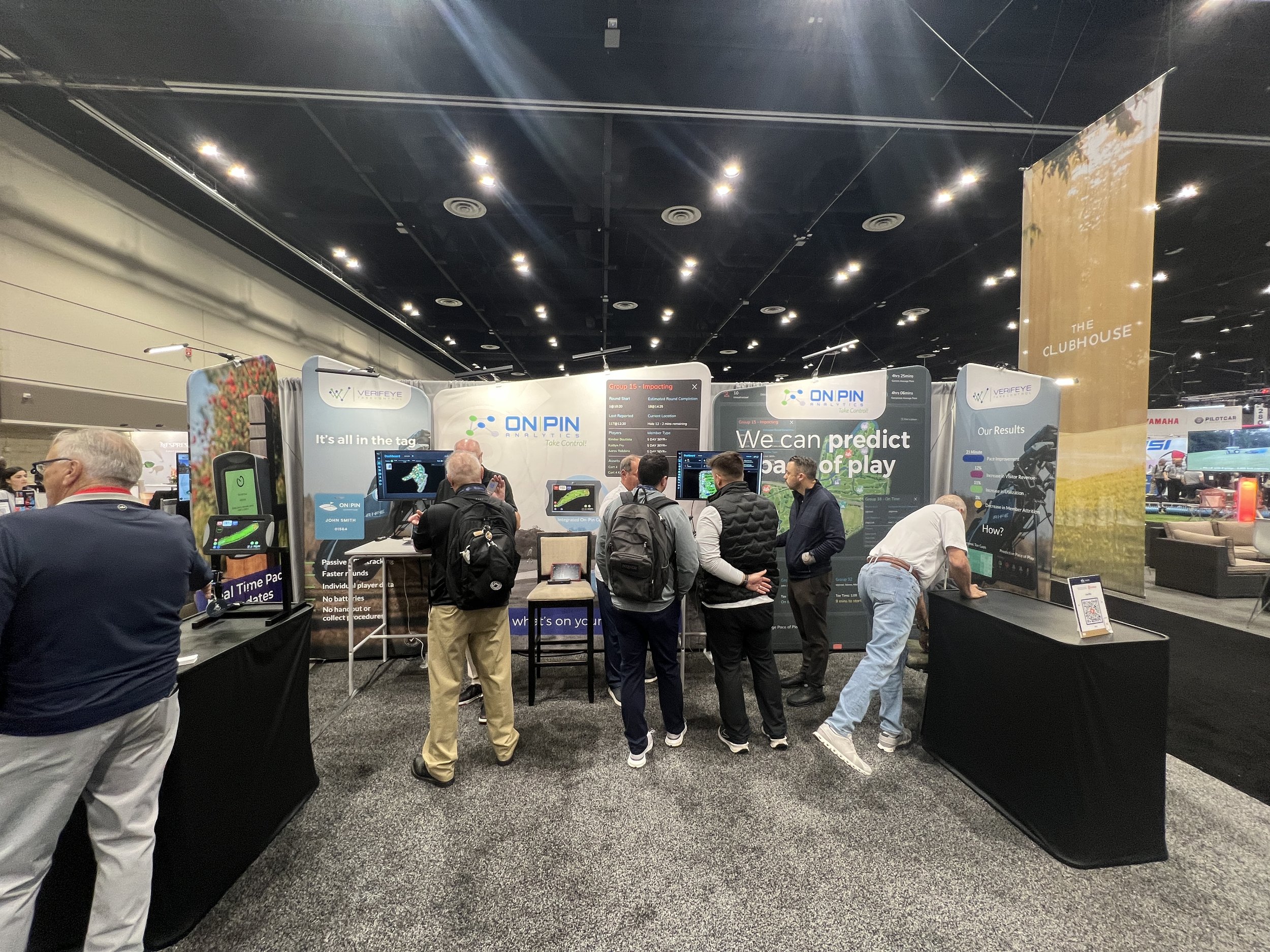 Trade show booth for ON PIN ANALYTICS displaying various screens and banners, with people interacting and observing the exhibits in a convention center.
