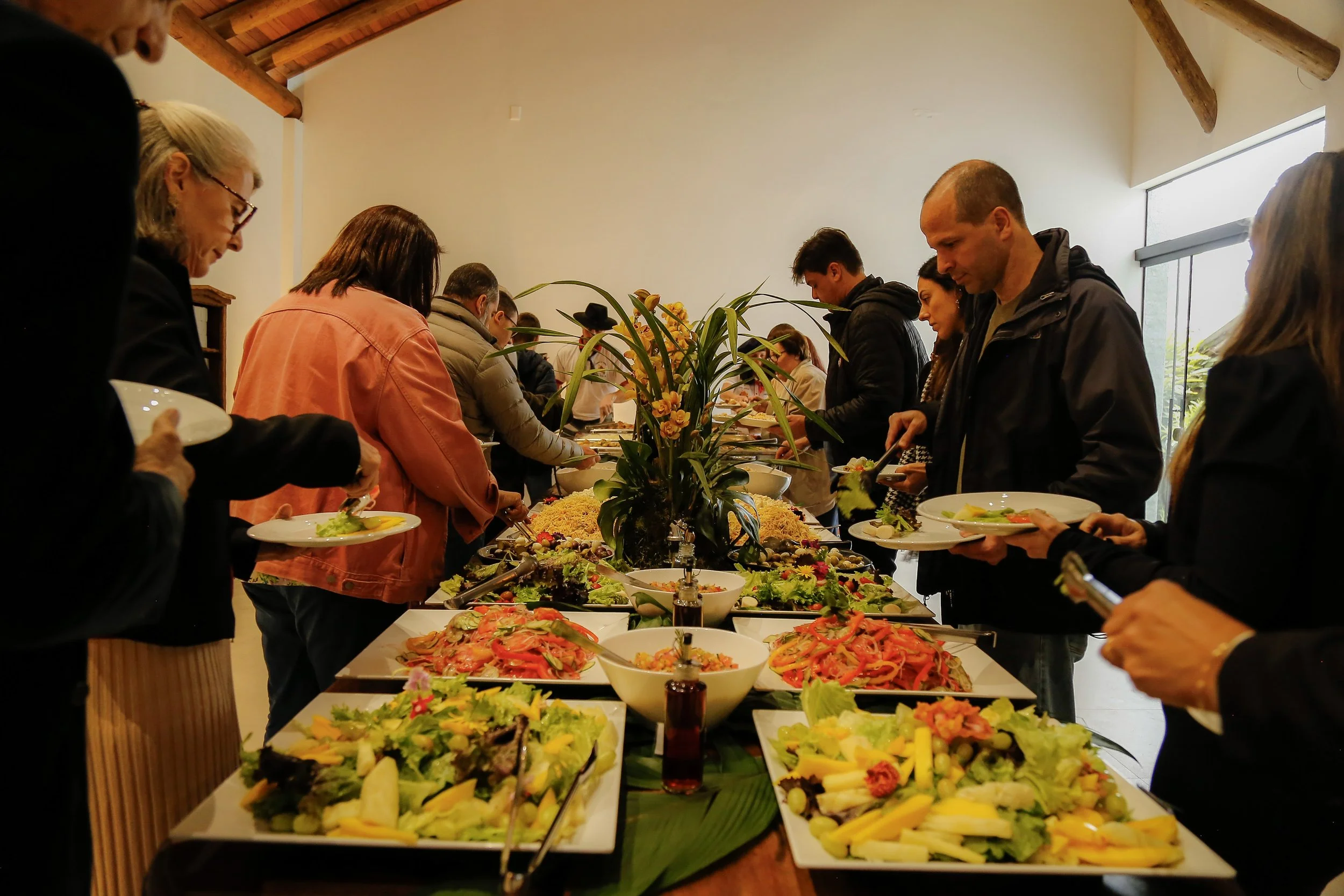 Pessoas servindo-se em uma estação de buffet com várias opções de saladas e pratos variados em uma celebração ou evento.