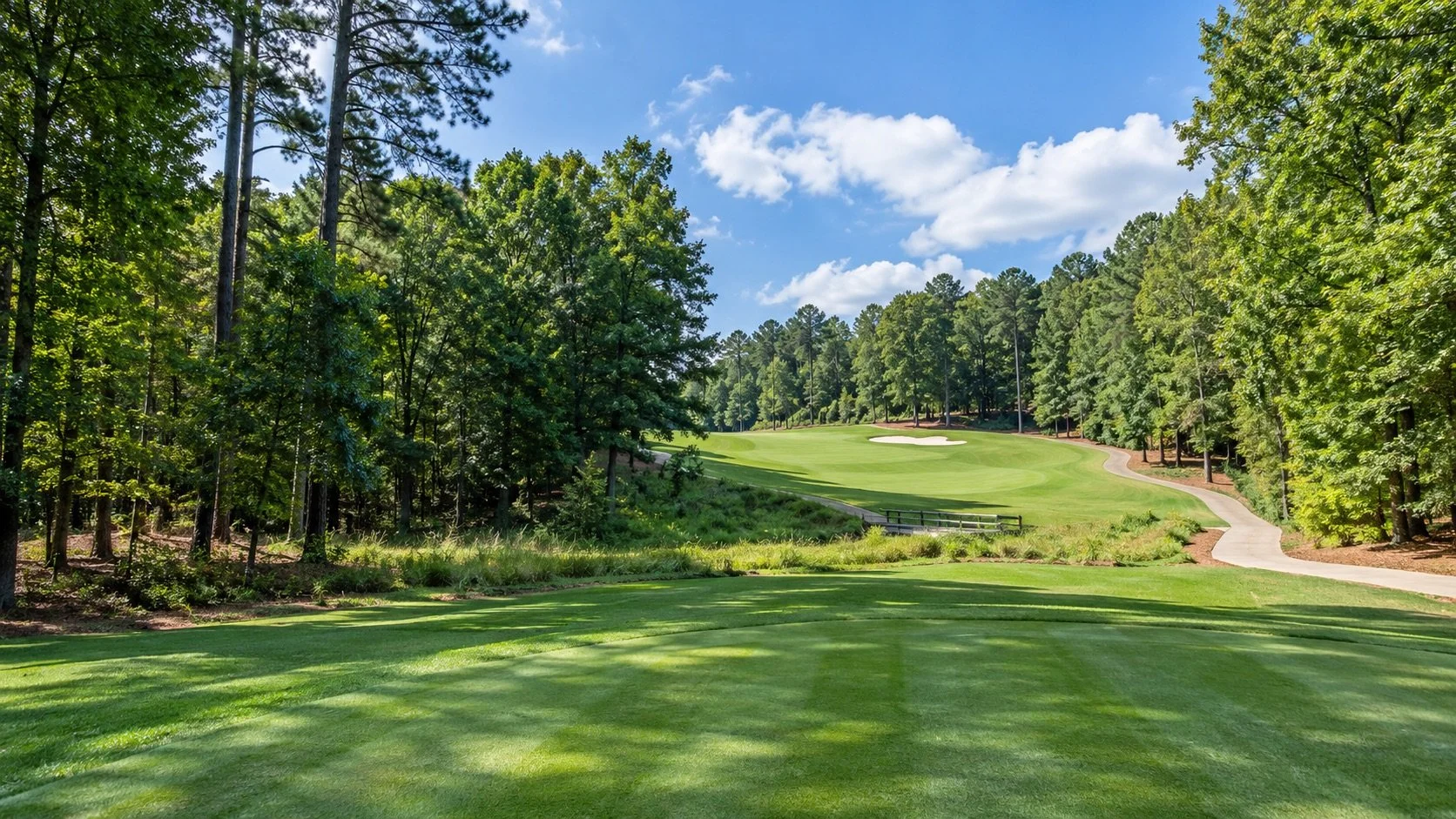 Tree-lined golf fairway rising to a green with a sand bunker, with a cart path and small footbridge, for golf communities in Forsyth County, Georgia