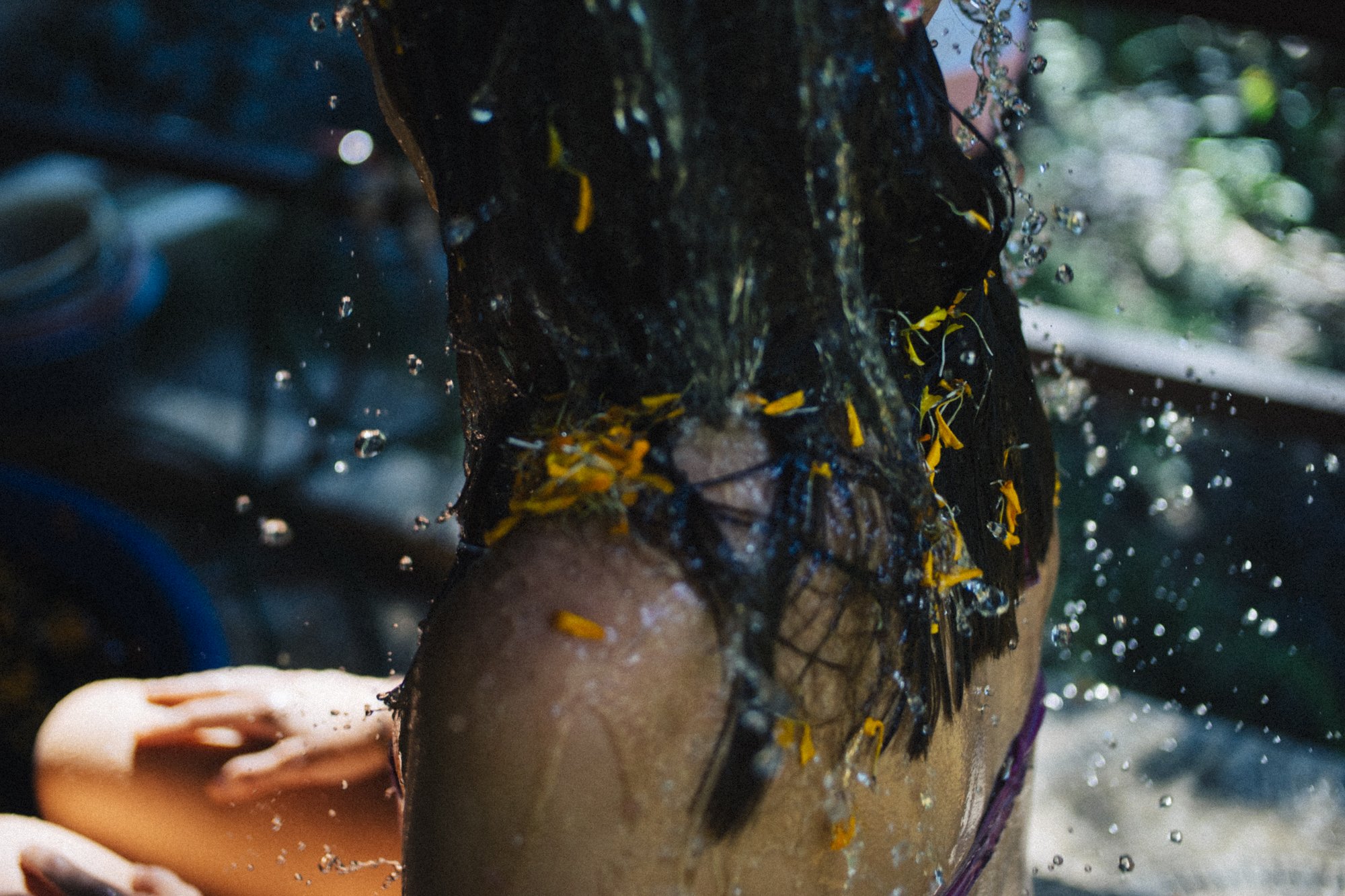 Child showering outdoors with water splashing around, dark hair visible.